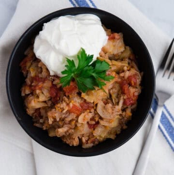 black bowl filled with cabbage roll sitting on top of napkin with fork to the side.