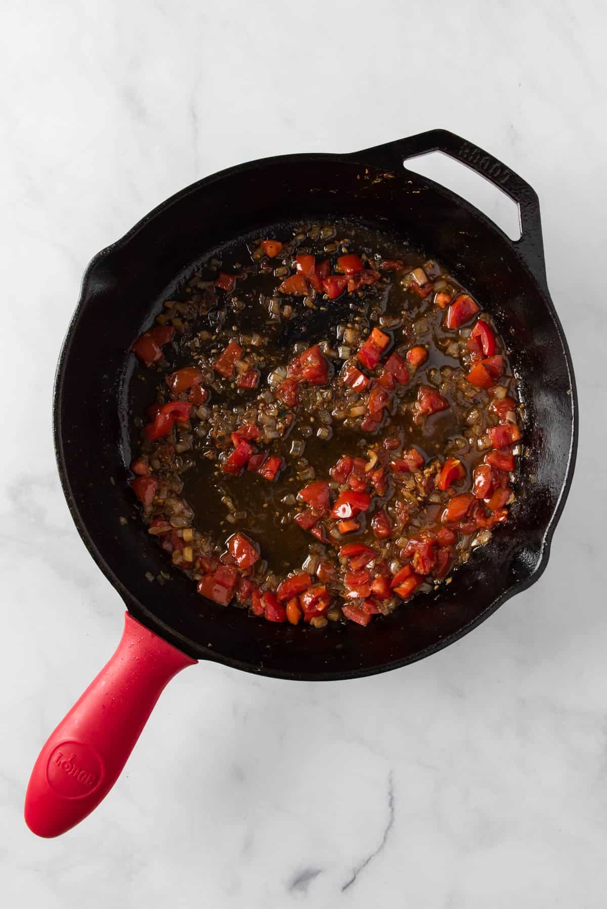 Sautéing tomatoes in a cast iron pan for veggie turkey meatballs in cream sauce.