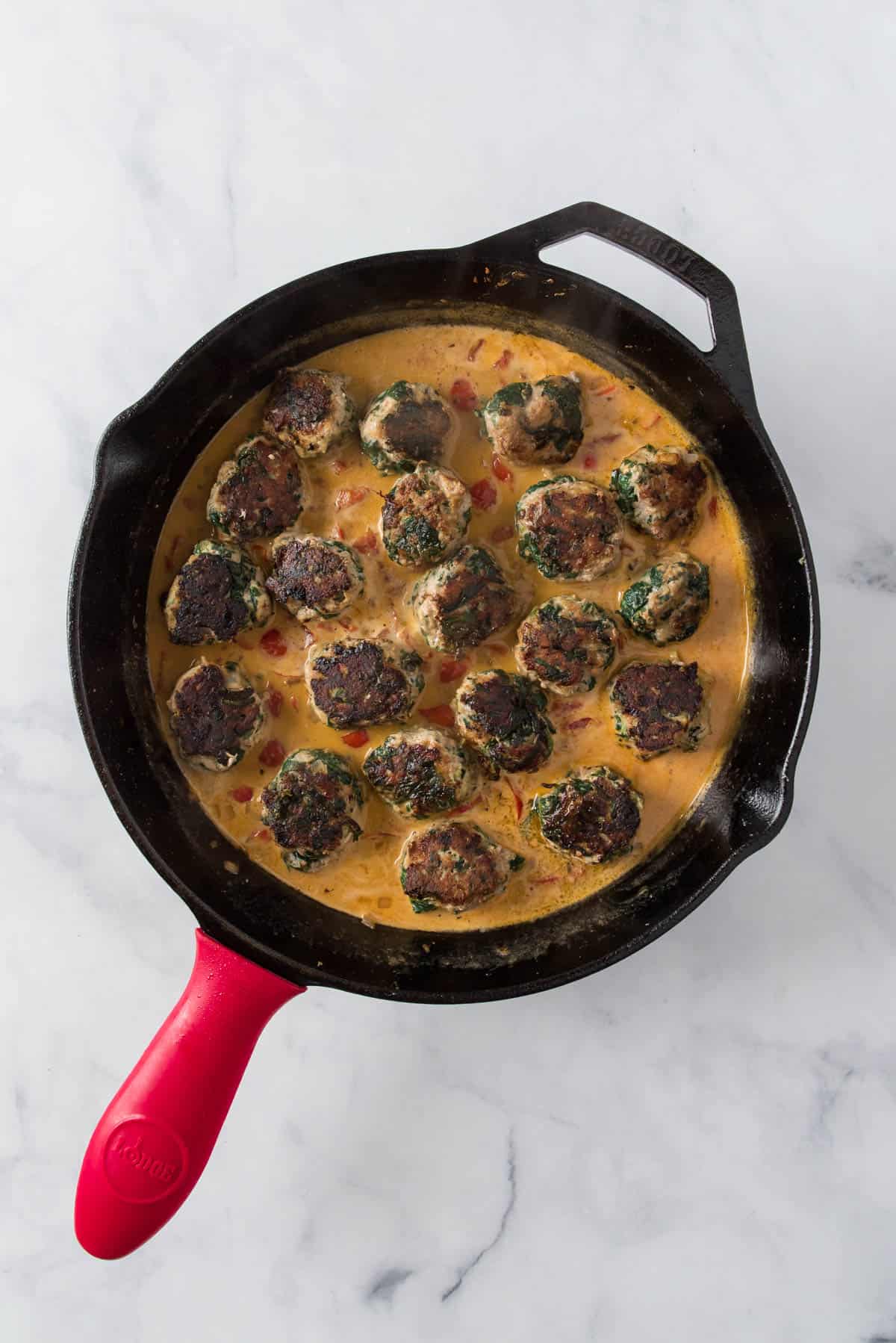 Veggie turkey meatballs simmering in sauce in a cast iron pan