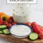 Homemade ranch dressing in a blue dish with a mason jar of ranch and veggies surrounding it on an olive wood board.