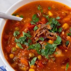 Hearty and delicious vegetable beef soup in a white bowl, topped with a sprinkle of parsley and a spoon in the left side of the bowl.