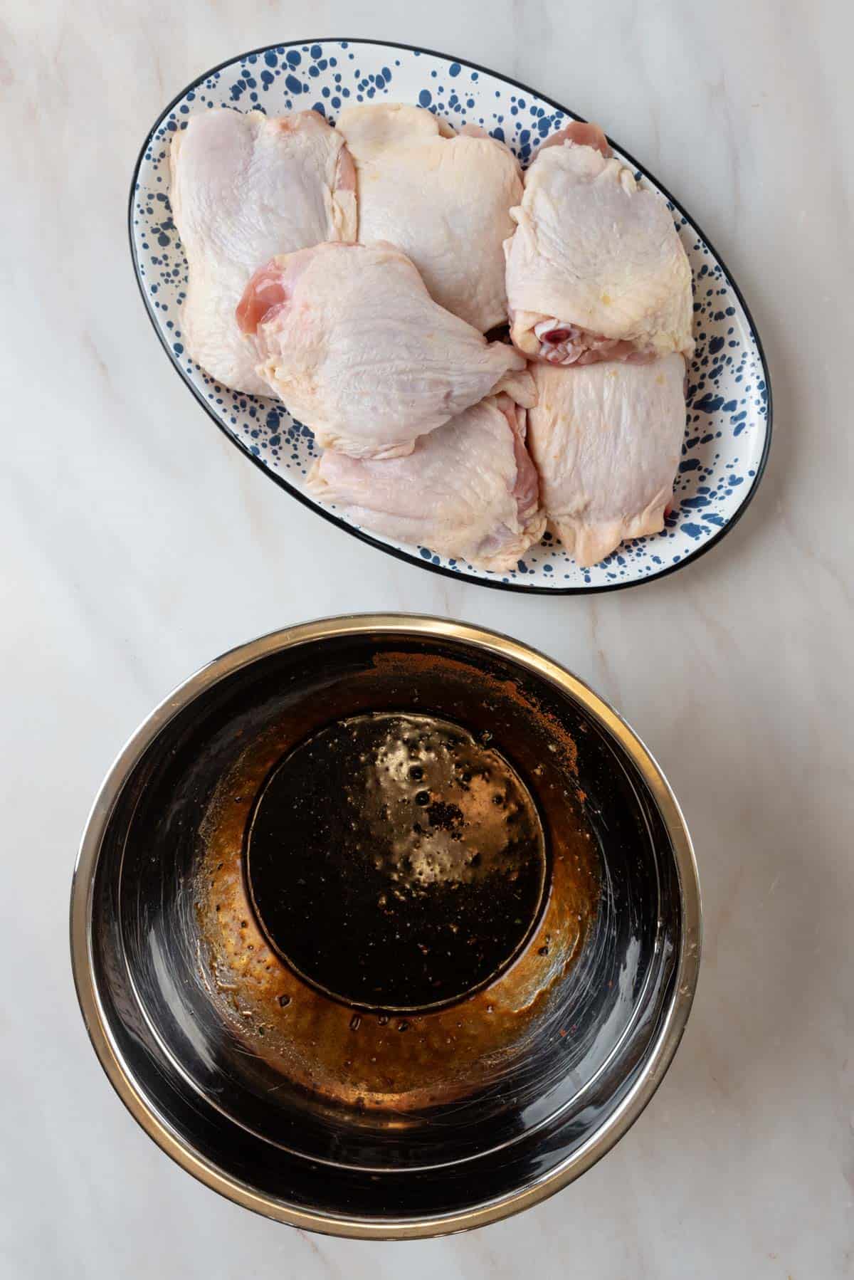 Balsamic marinade mixed in a large bowl with chicken thighs on a platter beside the bowl.