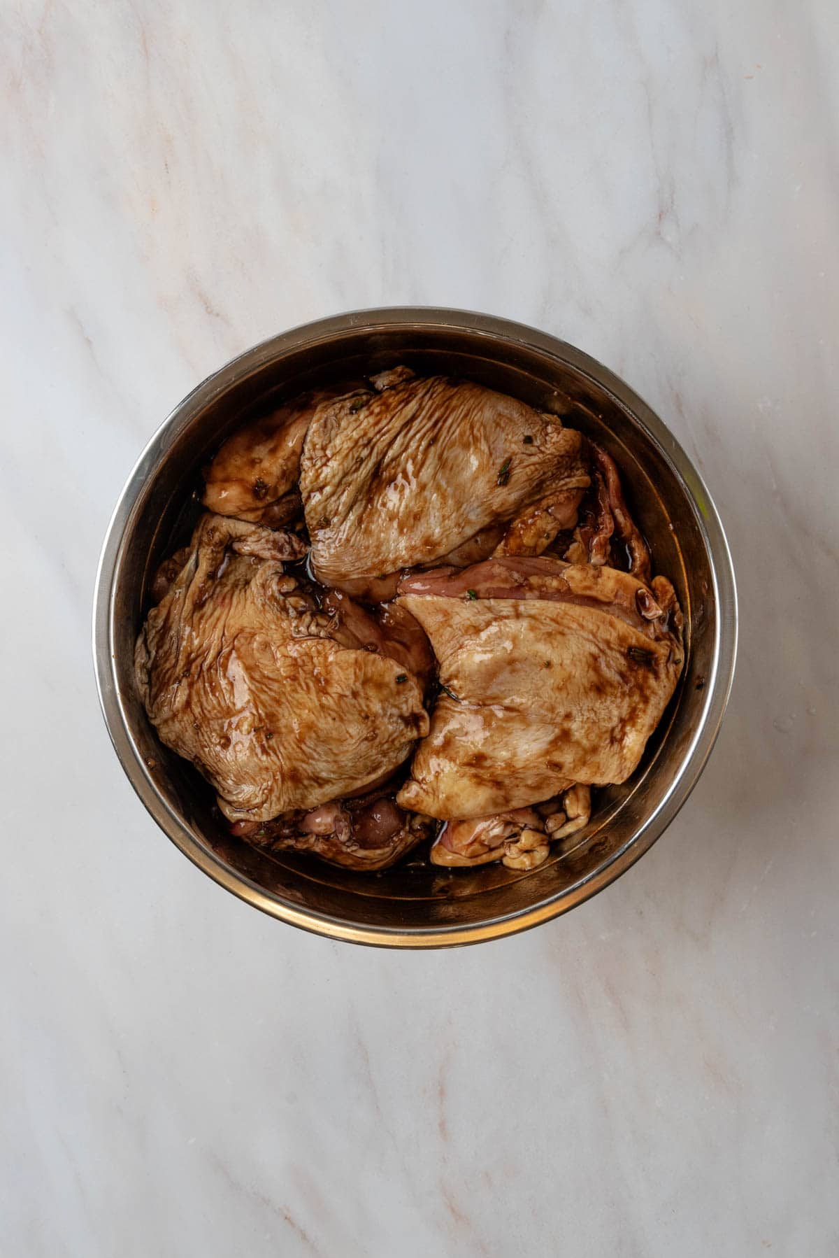 Chicken thighs marinading in a large stainless steel mixing bowl.