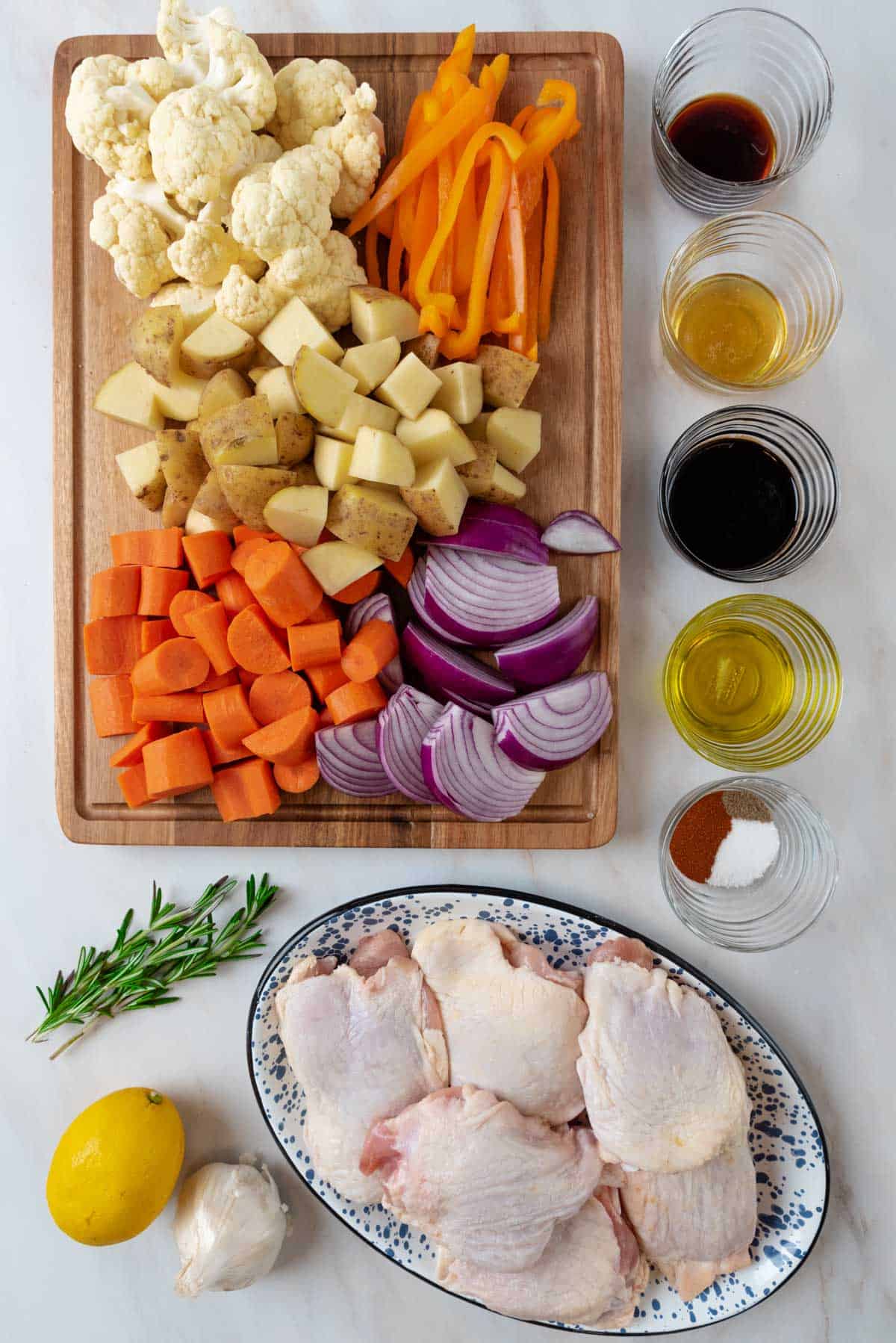 Ingredients for balsamic chicken thighs and vegetables on a marble background.