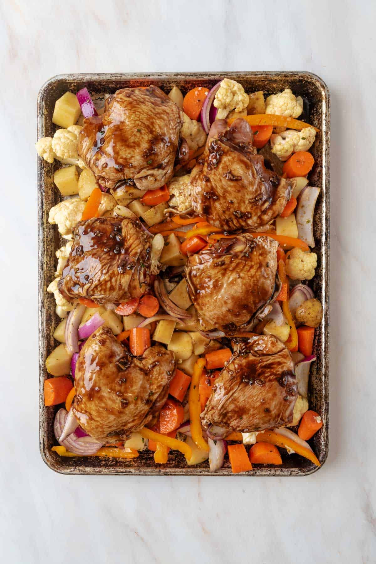 Seasoned vegetables on a sheet pan, topped with balsamic marinated chicken thighs.