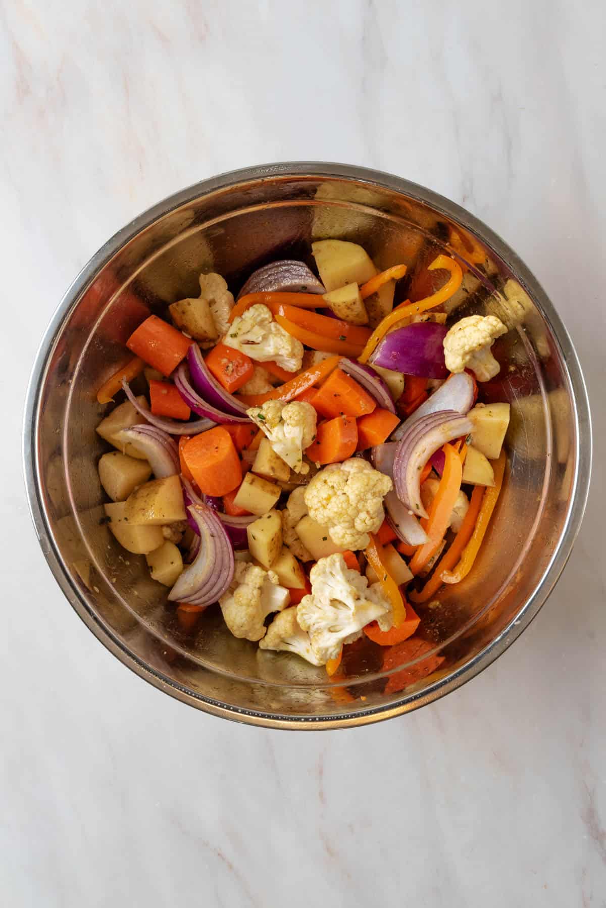 Chopped vegetables in a large mixing bowl, coated in olive oil and seasonings.