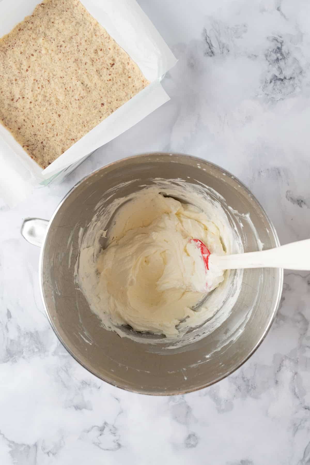Cream cheese filling layer with the whipped cream folded in, in a large stainless steel mixing bowl. A pan of shortbread crust beside it.