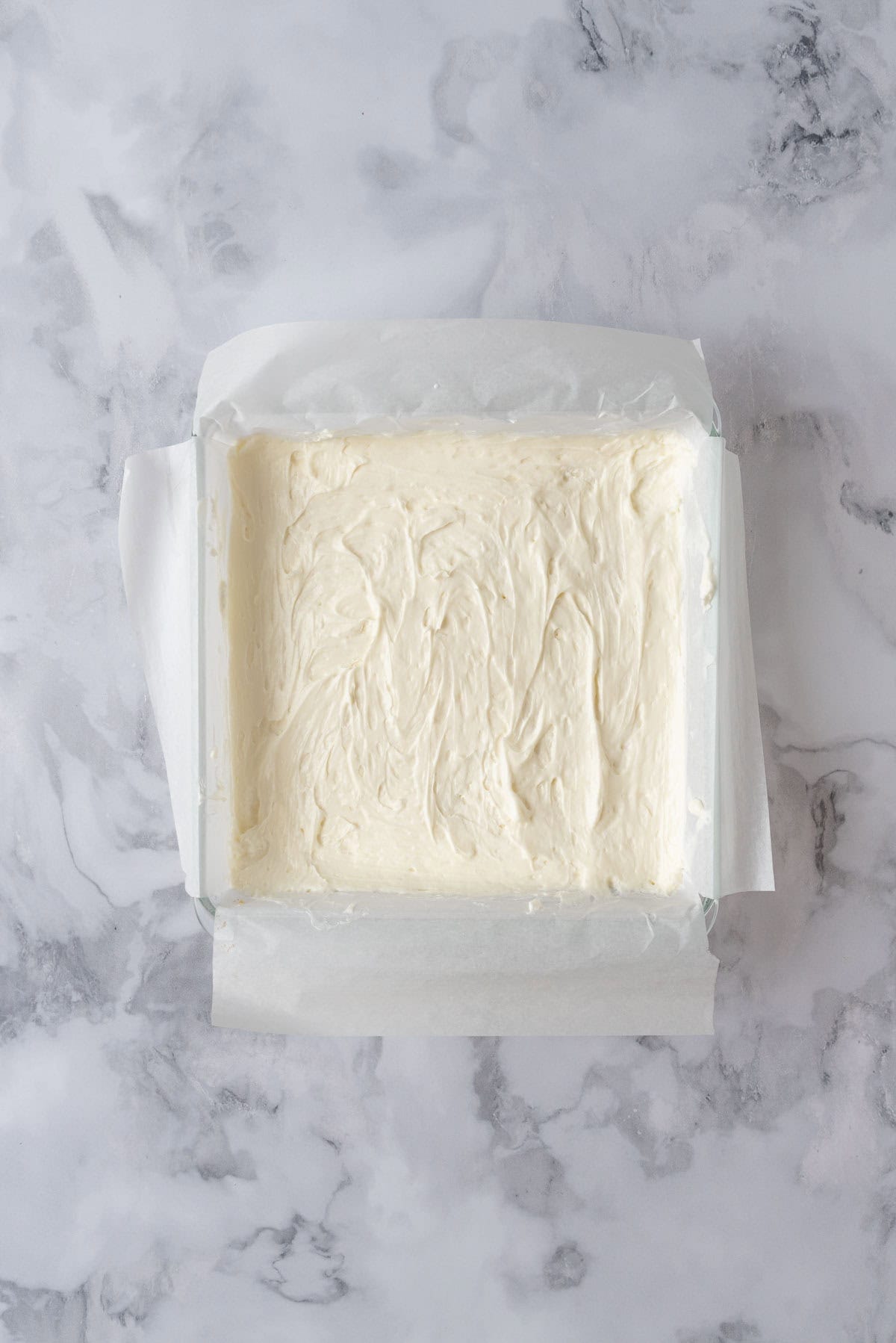 Cream cheese filling layer on top of a shortbread crust in a baking pan.