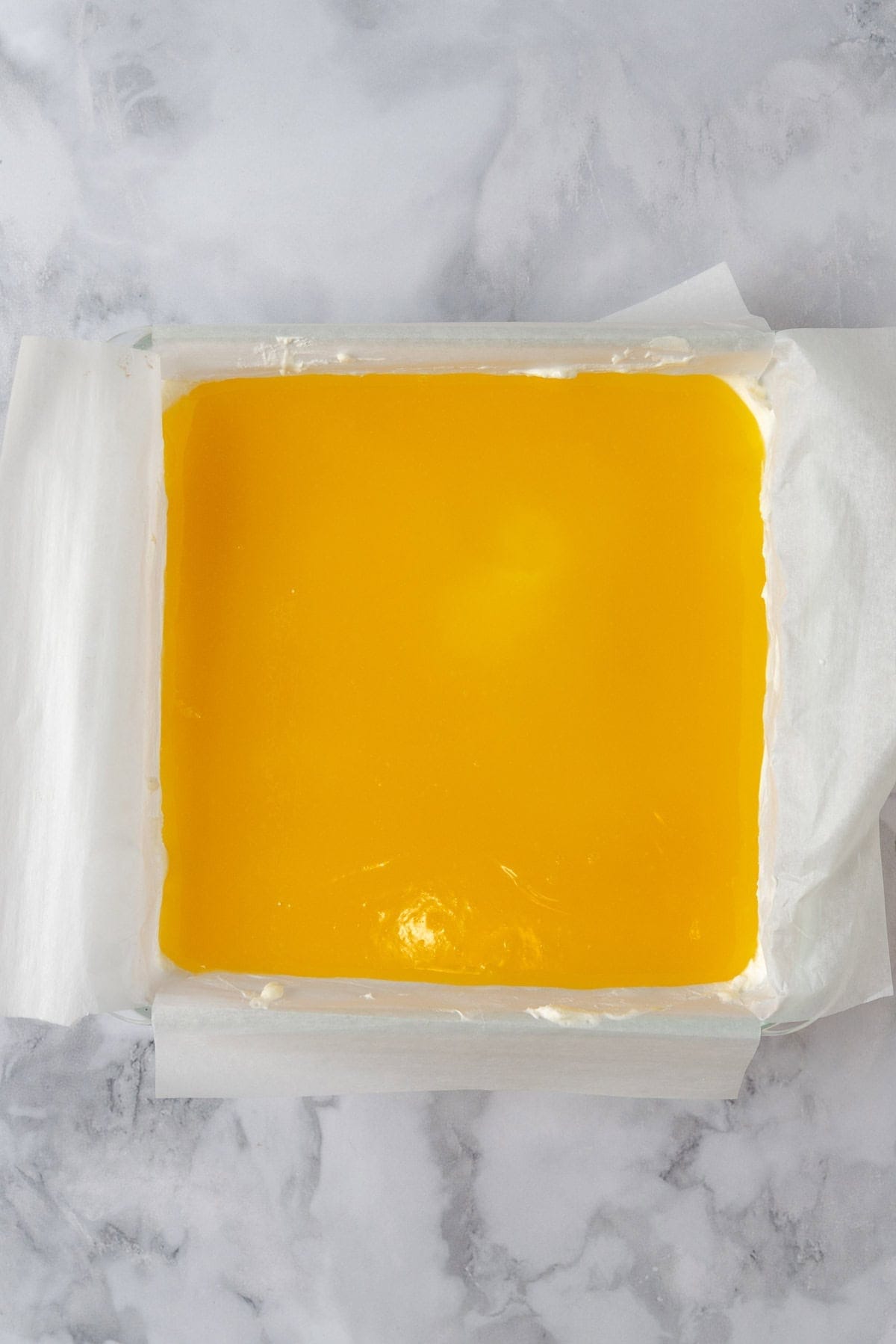 A baking dish with the lemon curd layer poured on top of the shortbread and cream cheese layers.