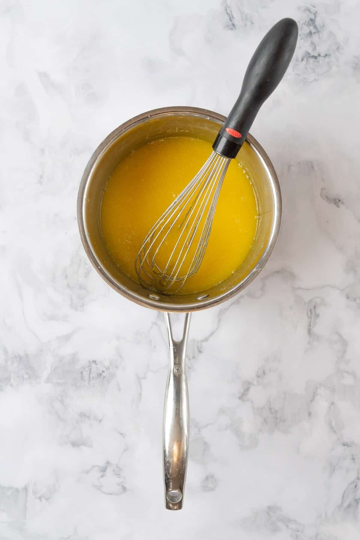 Lemon curd cooked in a small sauce pan with a whisk in the curd.