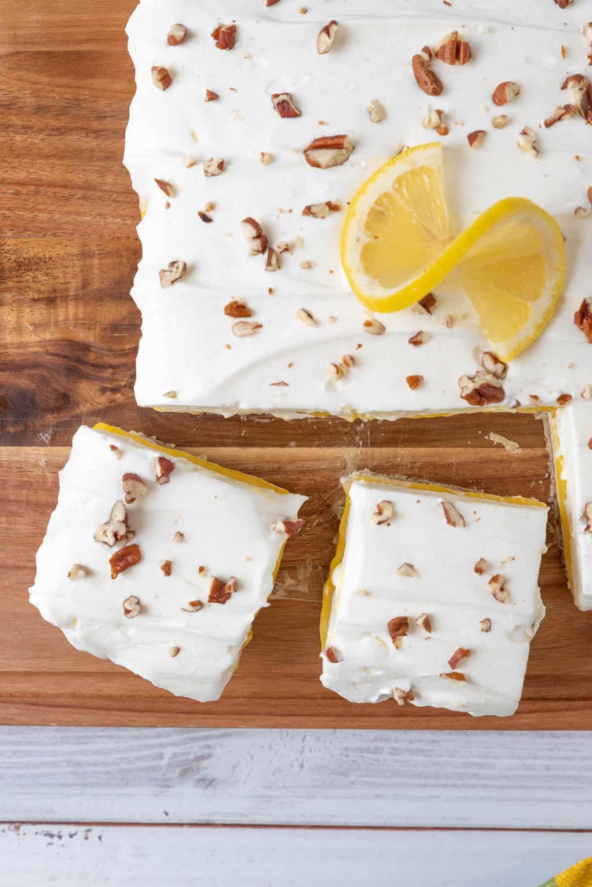 Two slices of Lemon Lush Dessert from Scratch on a wooden cutting board pulled away from the rest of the dessert, on top of a white wooden tabletop.