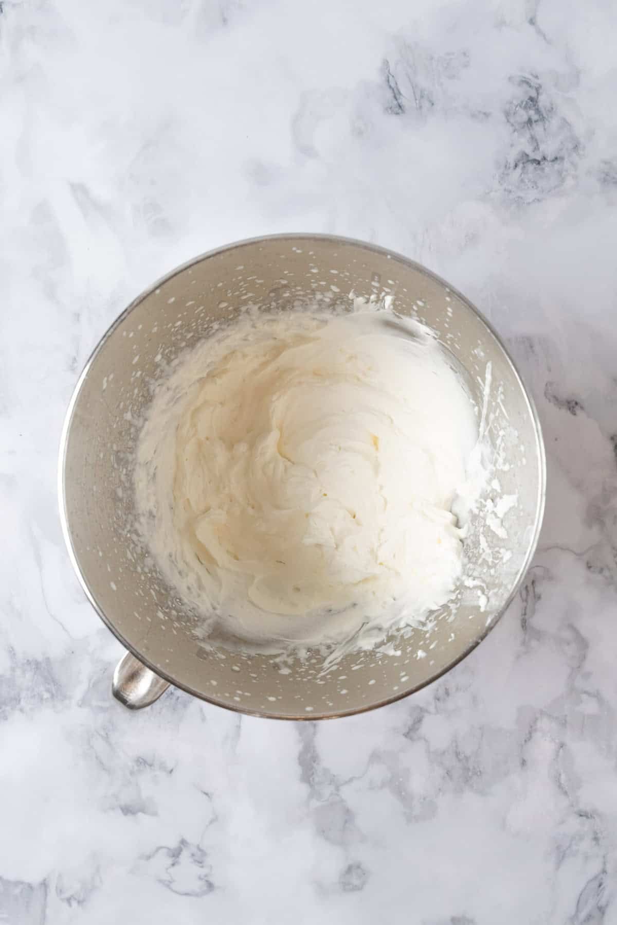 Whipped ream in a large stainless steel mixing bowl.