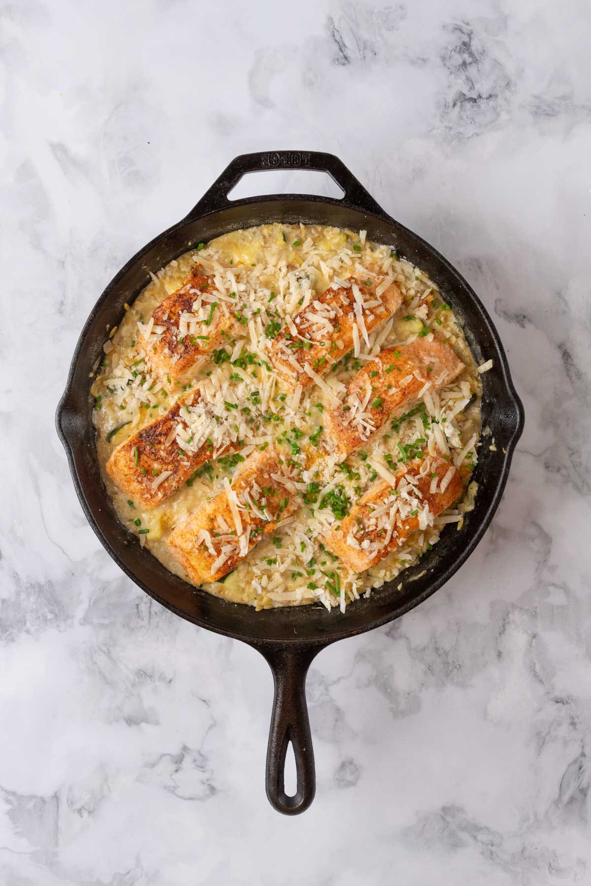 A finished cast iron skillet of Salmon & Orzo on a white marble background.