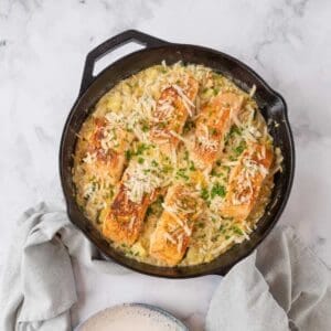 A cast iron skillet holding Salmon Orzo, garnished with parmesan cheese and chives.