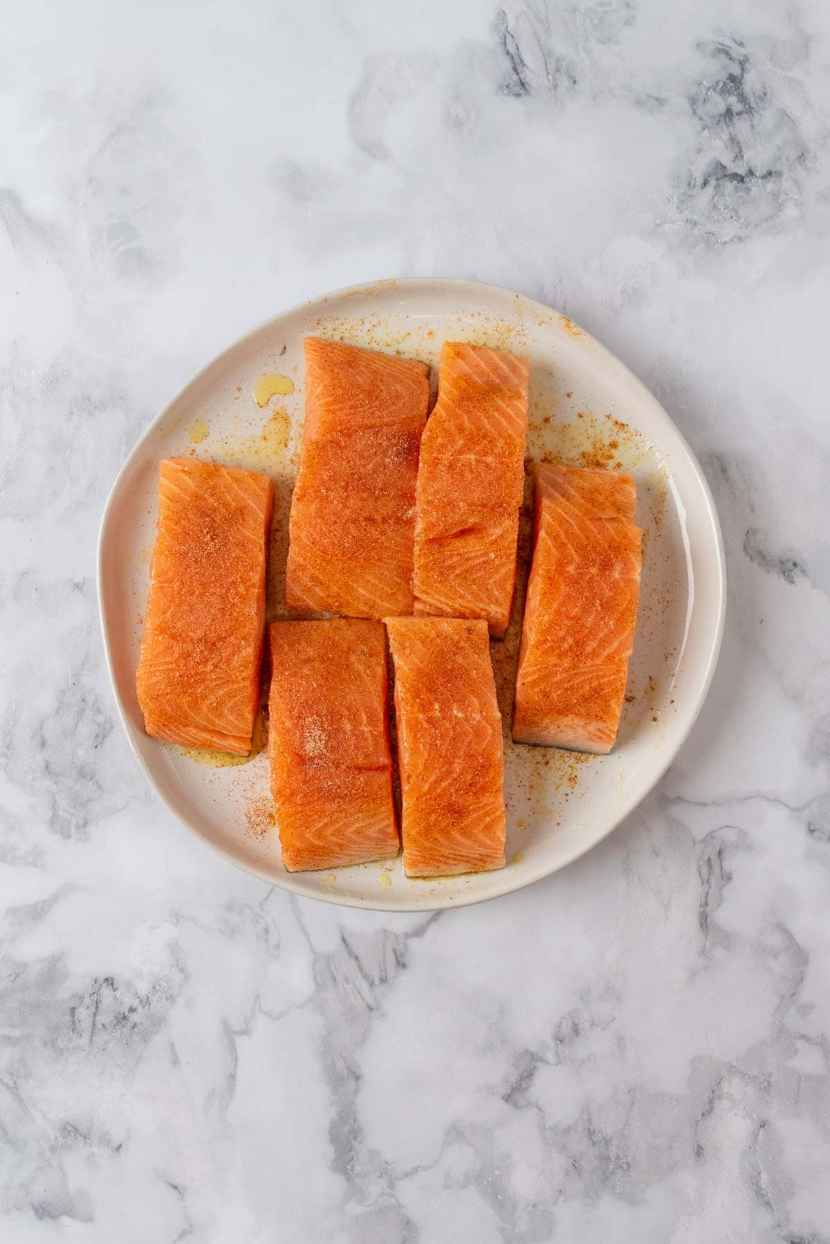Salmon fillets seasoned on a plate, ready to be cooked.