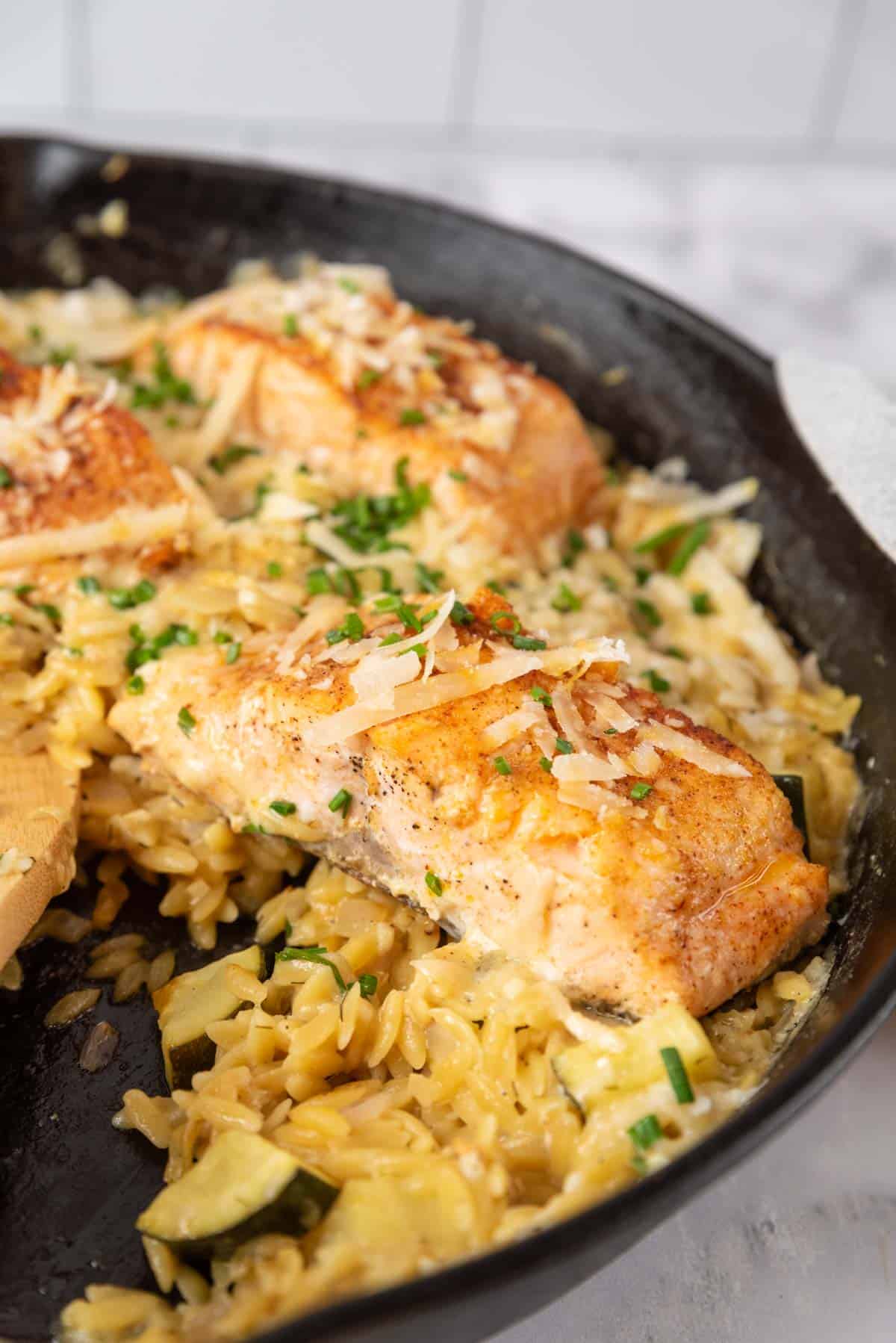 A closeup of salmon and orzo in a cast iron skillet.