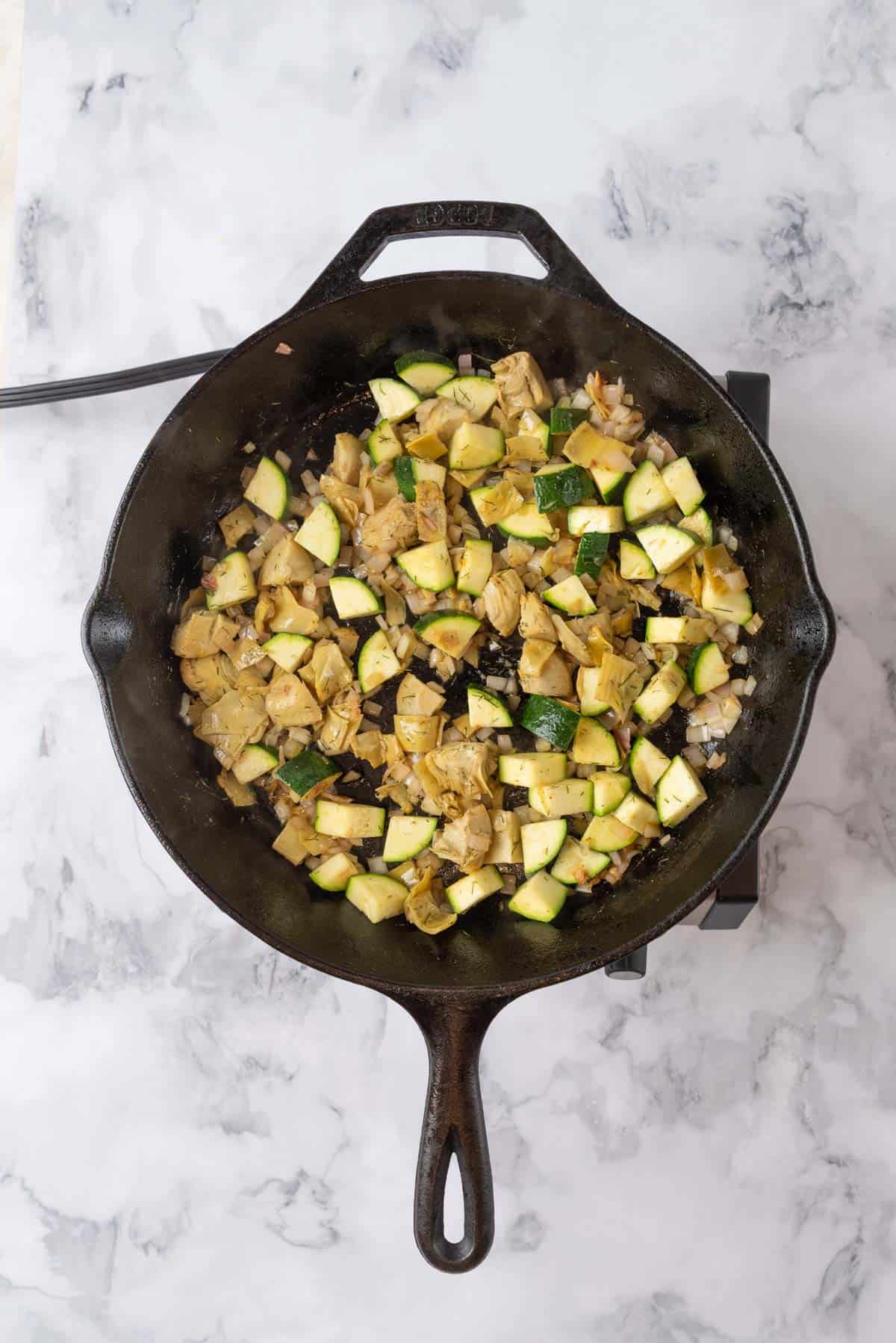 Shallot, zucchini and artichokes sautéing in a skillet.