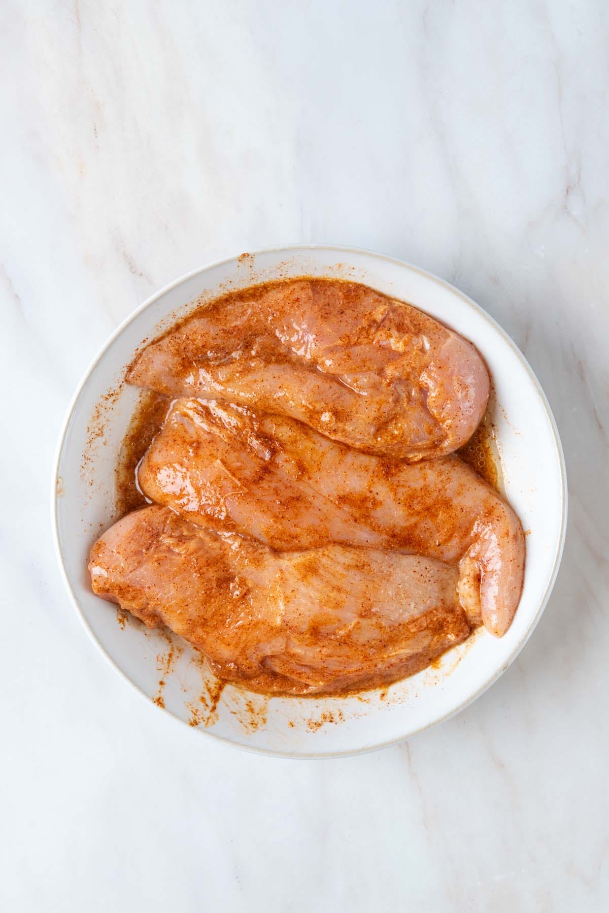 Chicken breast in marinade resting on a bowl.