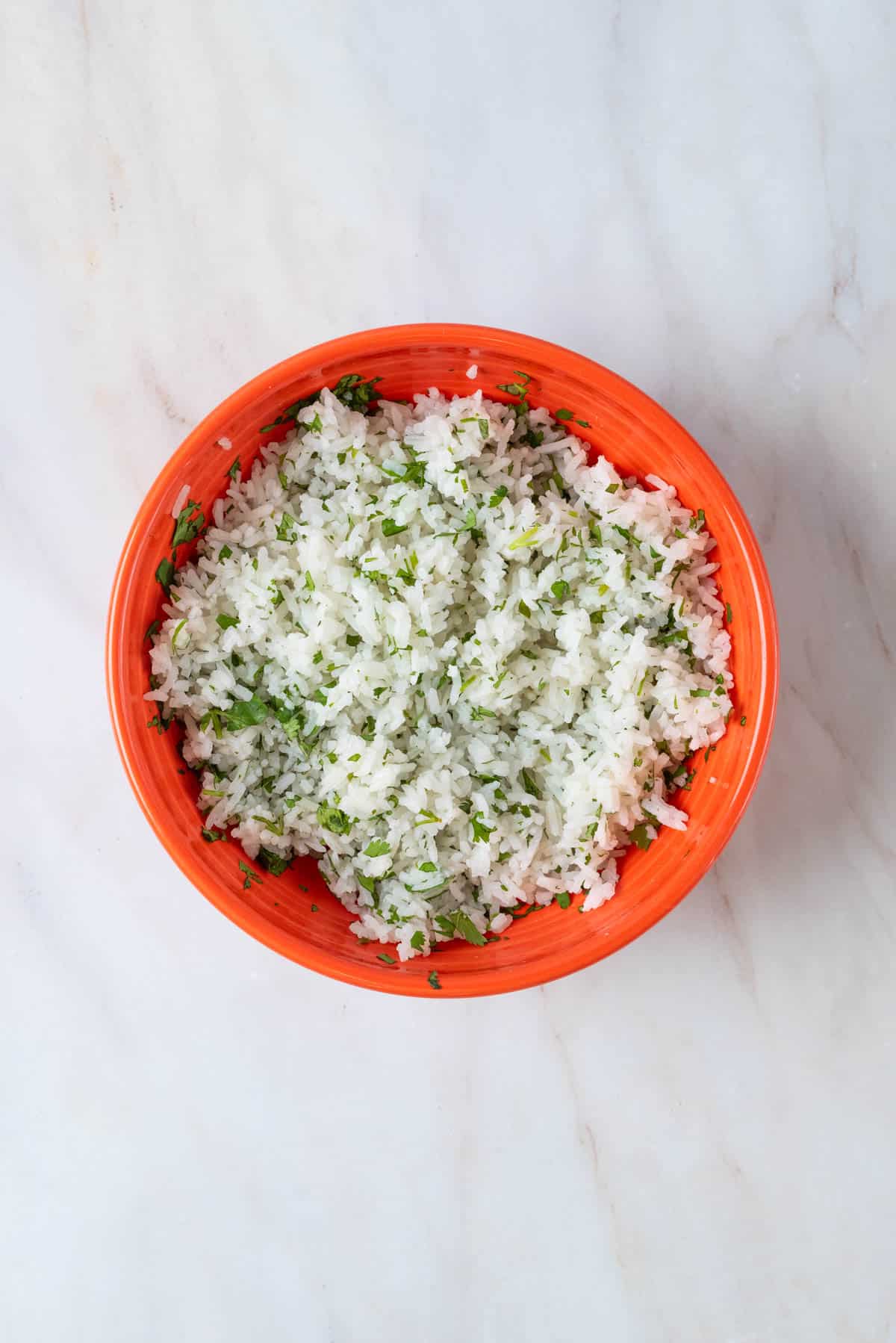 Jasmine rice with cilantro and lime juice in a bright orange bowl.