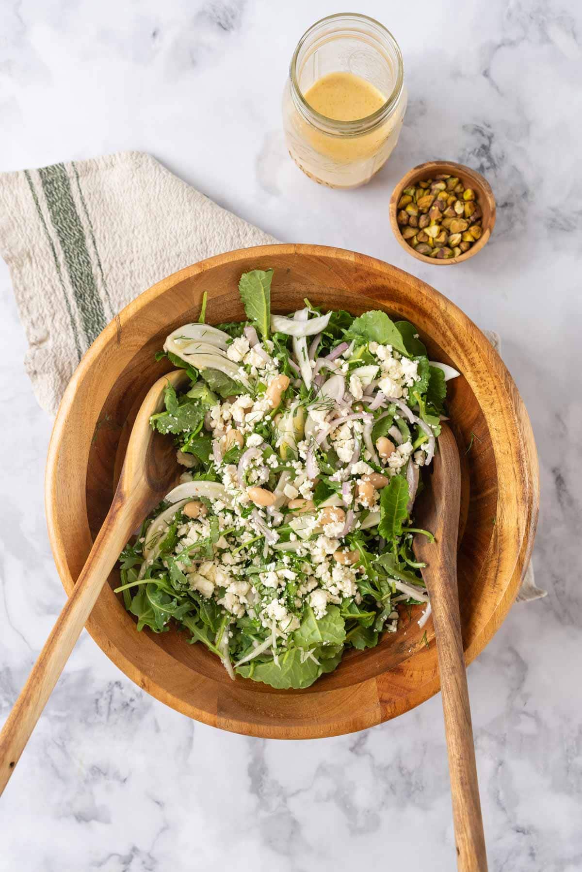 A large wooden salad bowl with t wo wooden salad spoons and the salad ingredients ready to be gently tossed.