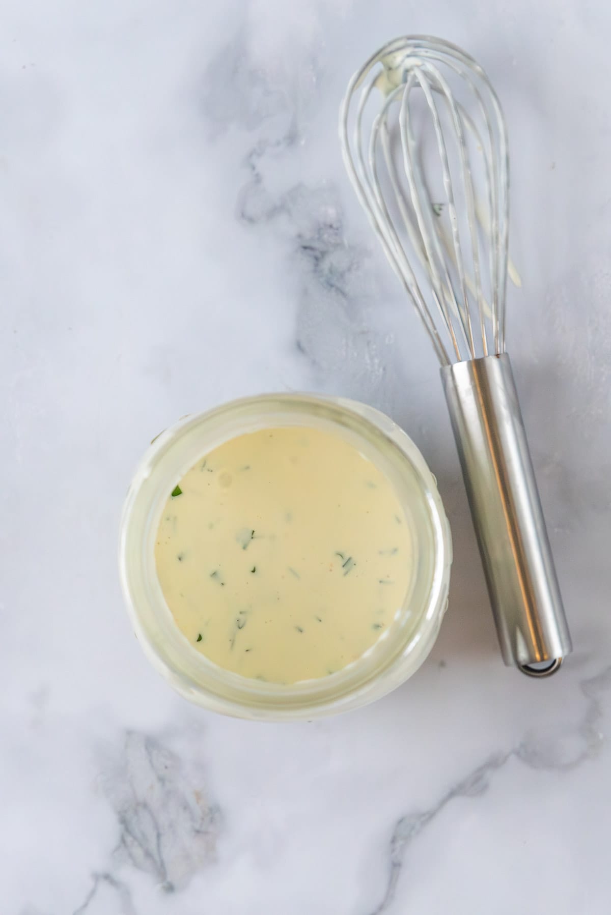 Creamy, zesty club salad dressing in a mason jar on a white marble countertop with a small whisk to the side.