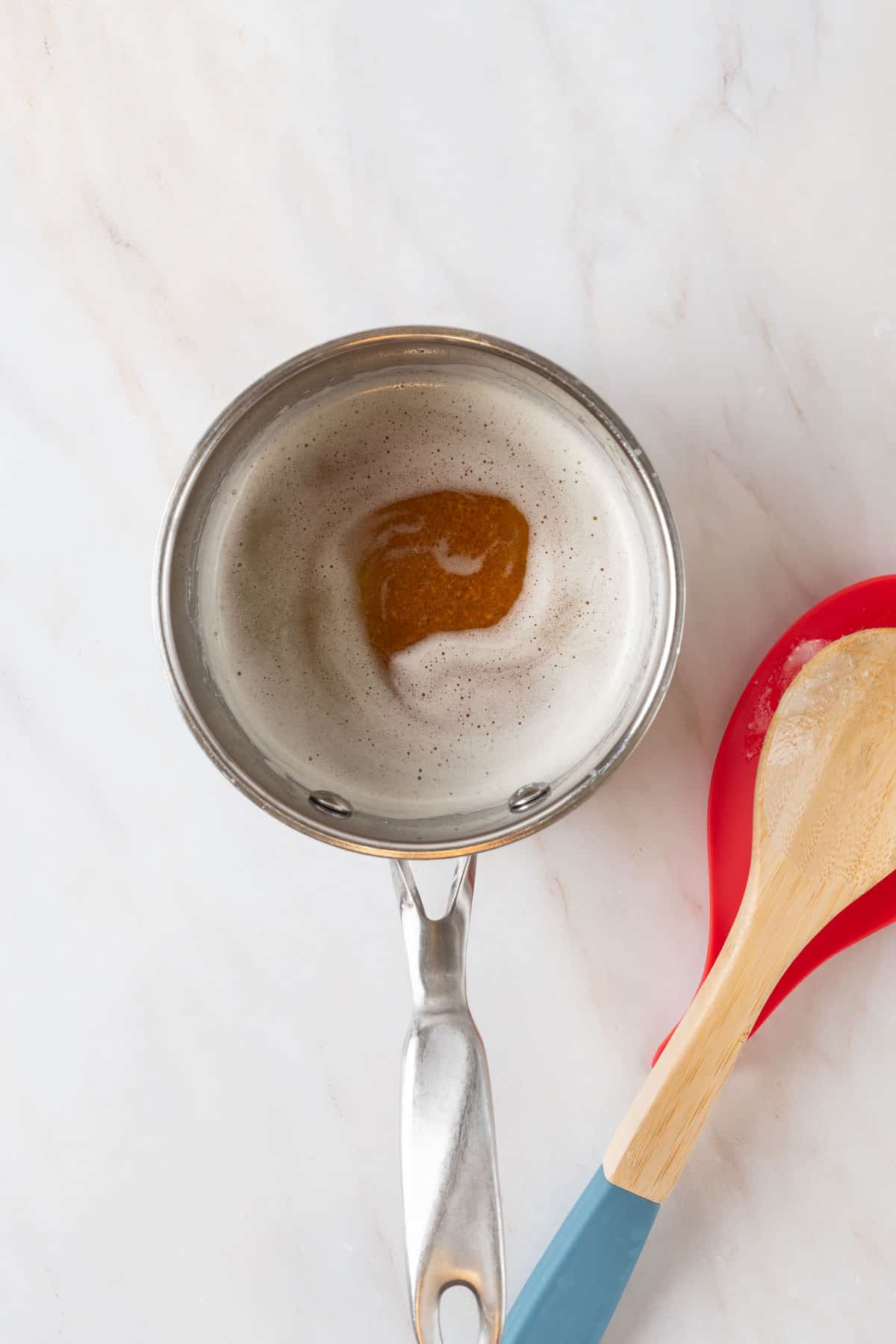 Brown butter in a small stainless steel sauce pan. A wooden spoon rests beside the pan on a red spoon rest.