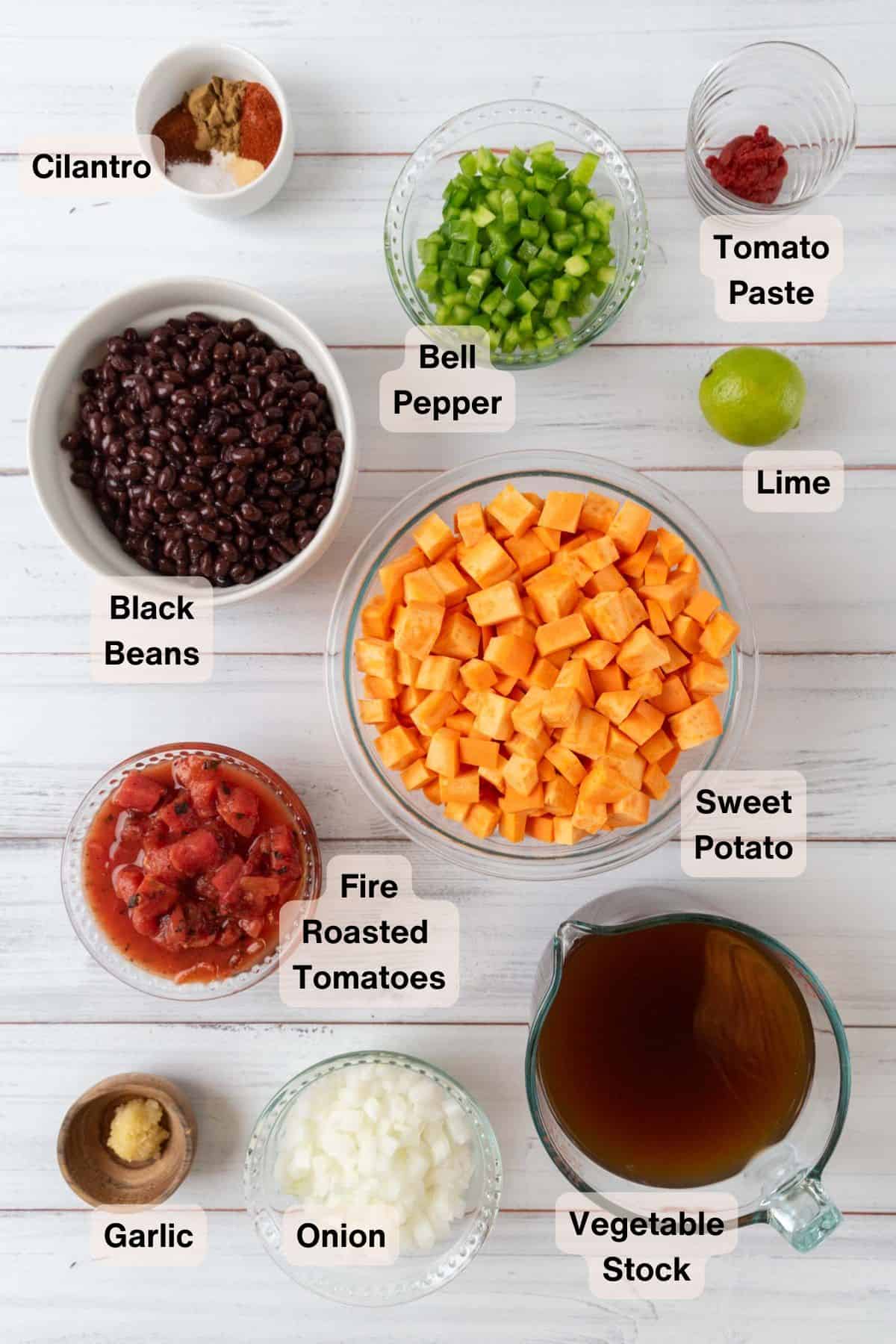 Ingredients for Sweet Potato Black Bean Soup in various bowls and dishes on a white wooden tabletop.
