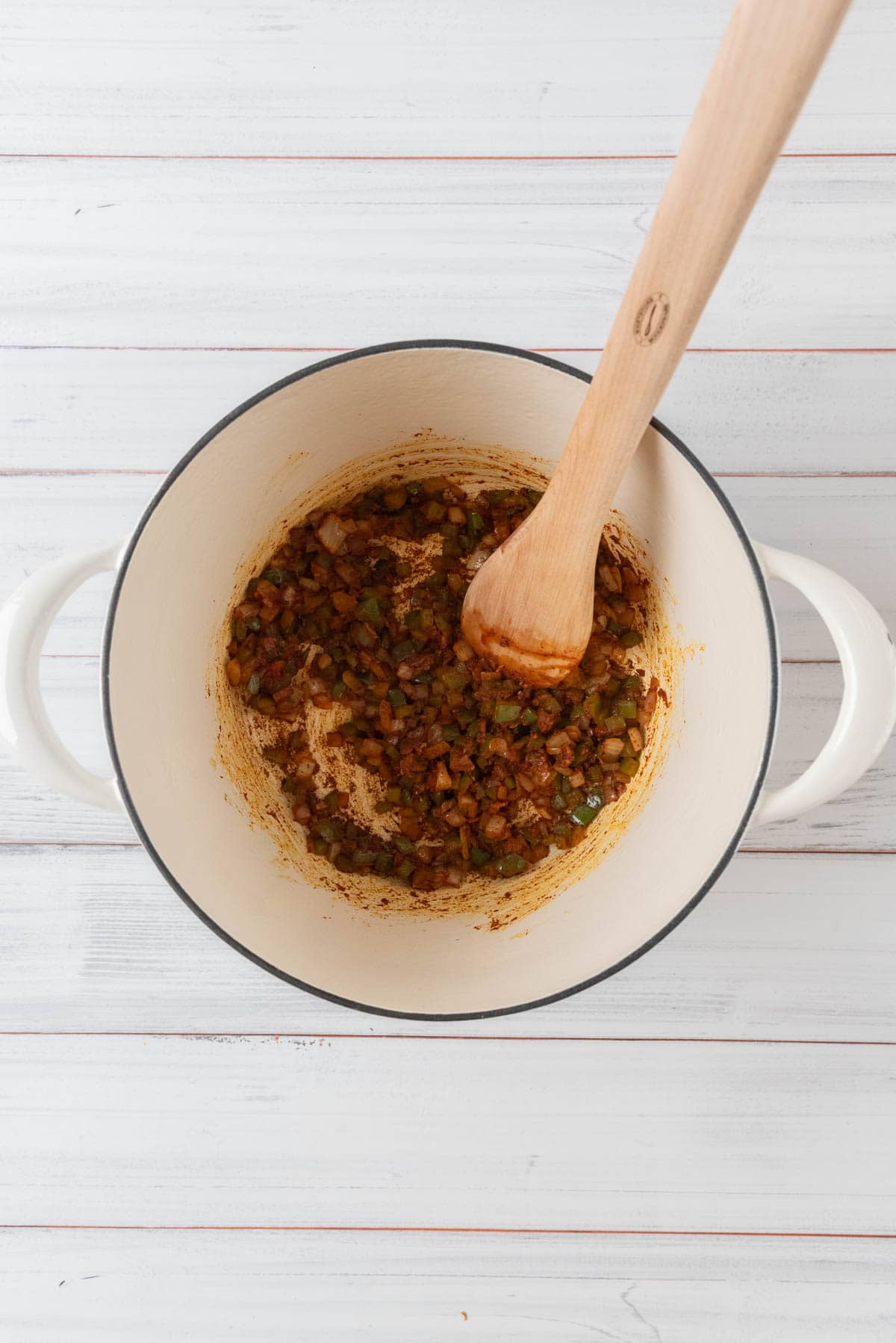 Seasonings being bloomed with the aromatics in a white Dutch oven.