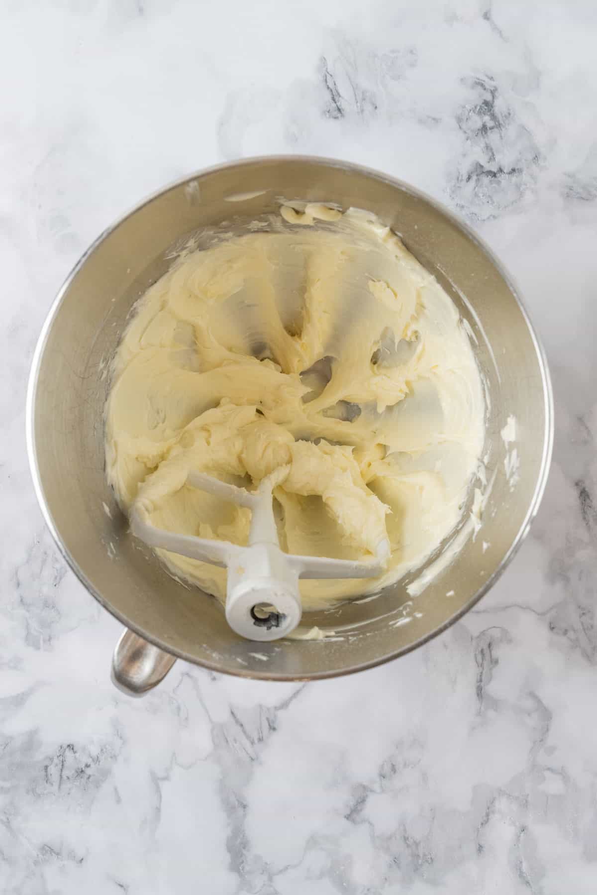 Butter and sugar creamed in a large stainless teel mixing bowl on a white marble countertop.