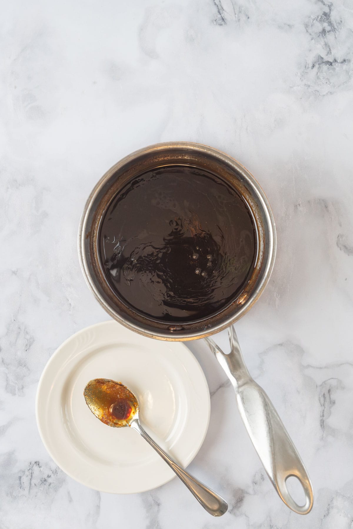 Hot honey glaze cooked down in a small saucepan, resting on a white marble countertop.