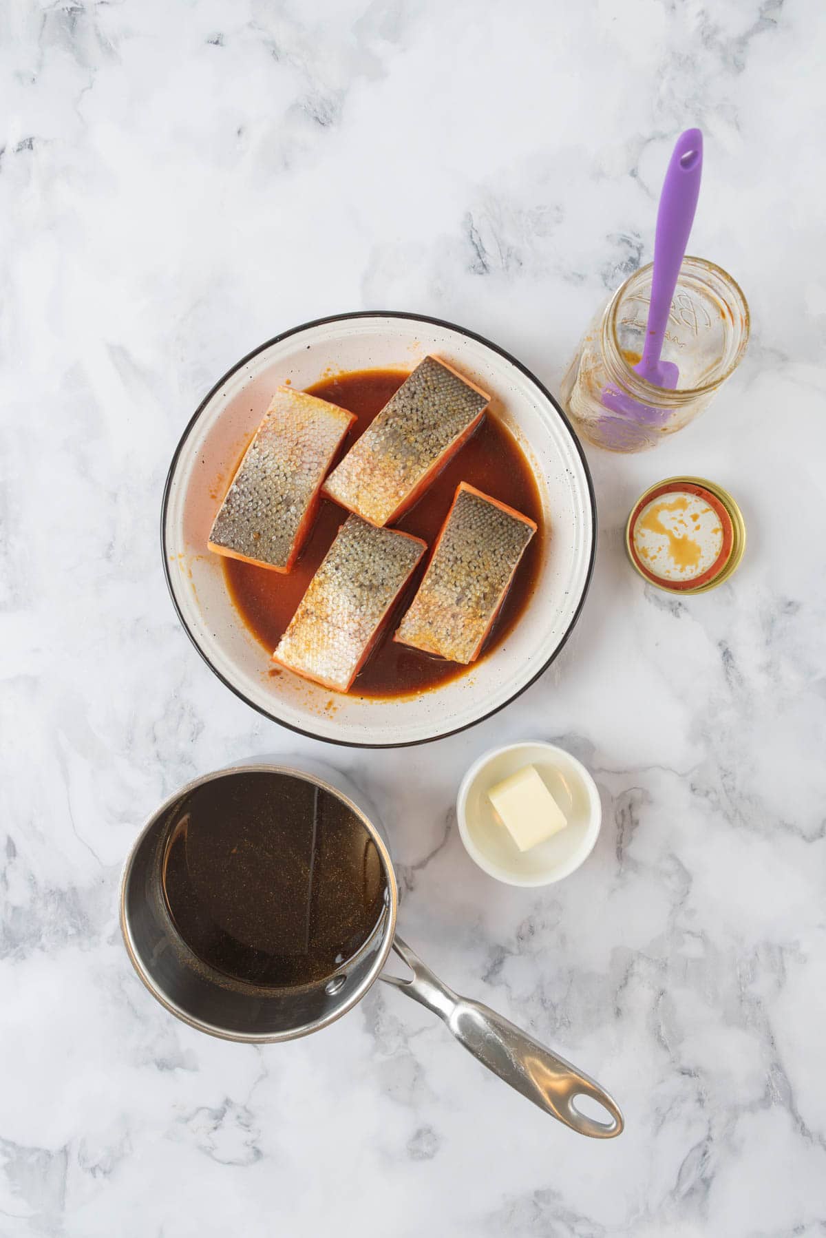 Salmon marinating on a serving platter with an empty marinade jar. A sauce pot with marinade ready to be cooked down into a hot honey glaze.