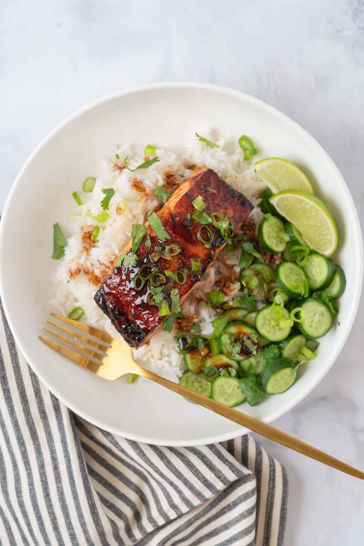 Hot honey glazed air fryer salmon plated with rice and cucumber, garnished with more glaze, chopped cilantro and green onions.