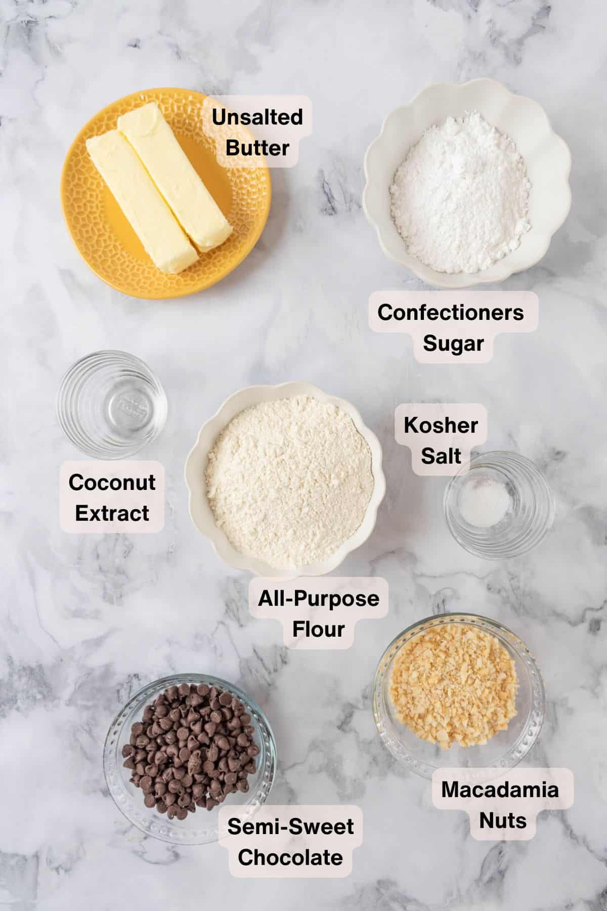 Macadamia nut shortbread cookie ingredients in small bowls on a white marble coutnertop.