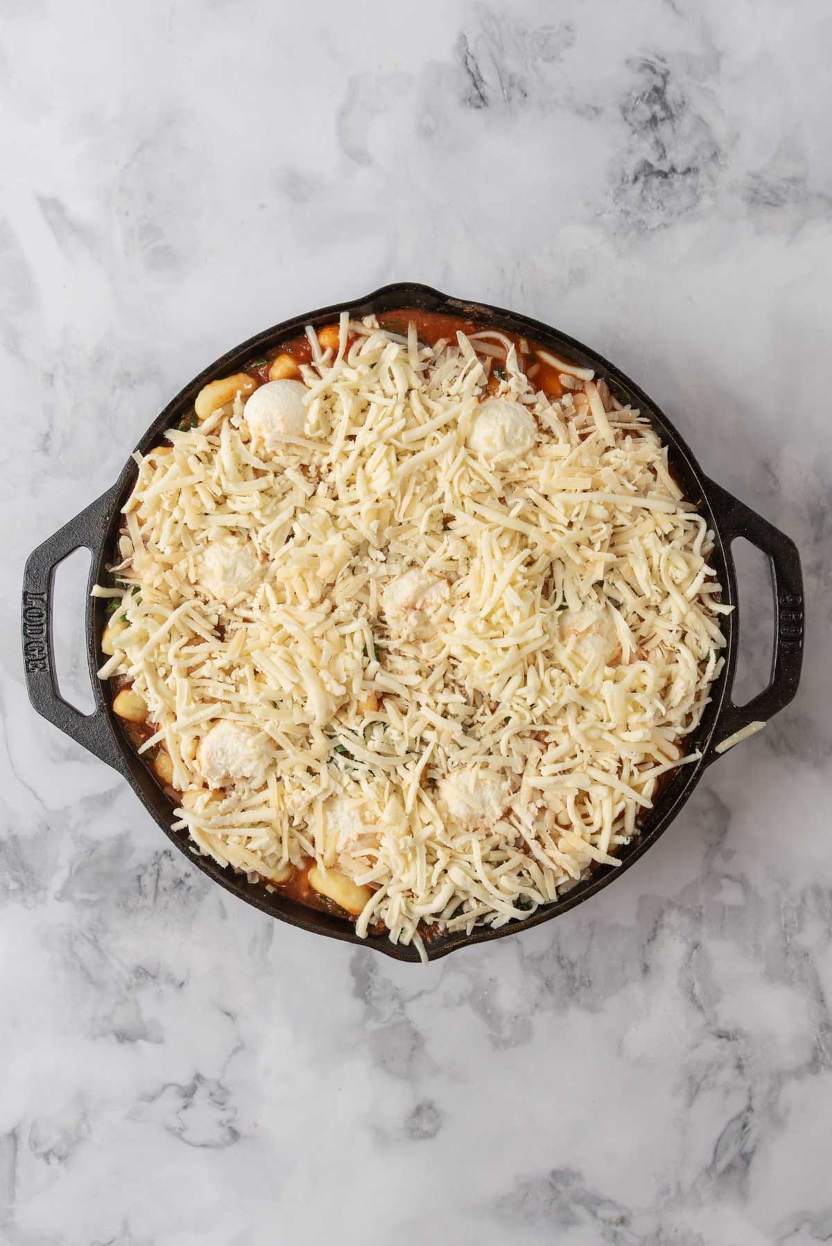 The cheese layer added to the top of a cast-iron skillet filled with baked gnocchi.