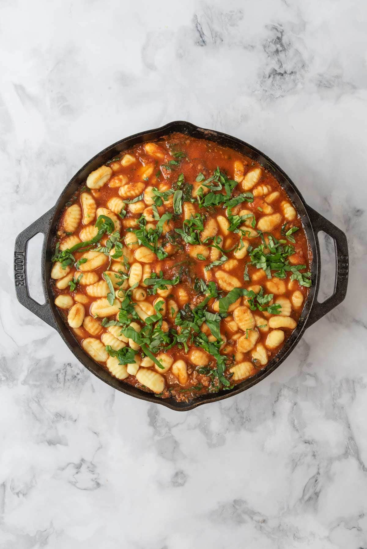 Gnocchi and ribbons of basil nestled into sausage and spinach tomato sauce in a cast-iron skillet.