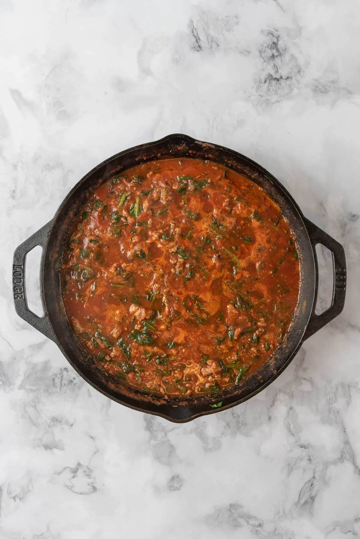 Tomato sauce with sausage and spinach simmering in a cast-iron skillet.