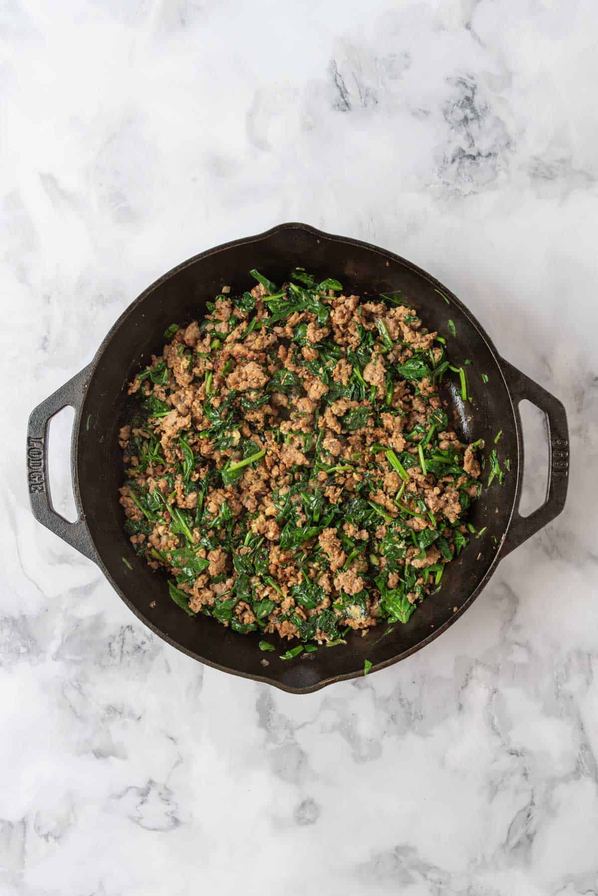 Browned sausage, spinach, onions and garlic sauteed in a cast-iron skillet.
