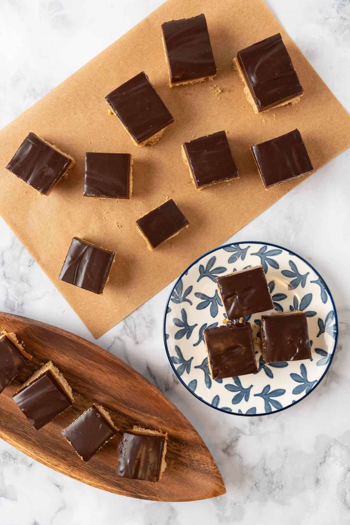 Chocolate espresso bars cut and plated on a blue and white plate with more to the side, scattered on a sheet of brown parchment paper and a wooden serving platter with four bars.