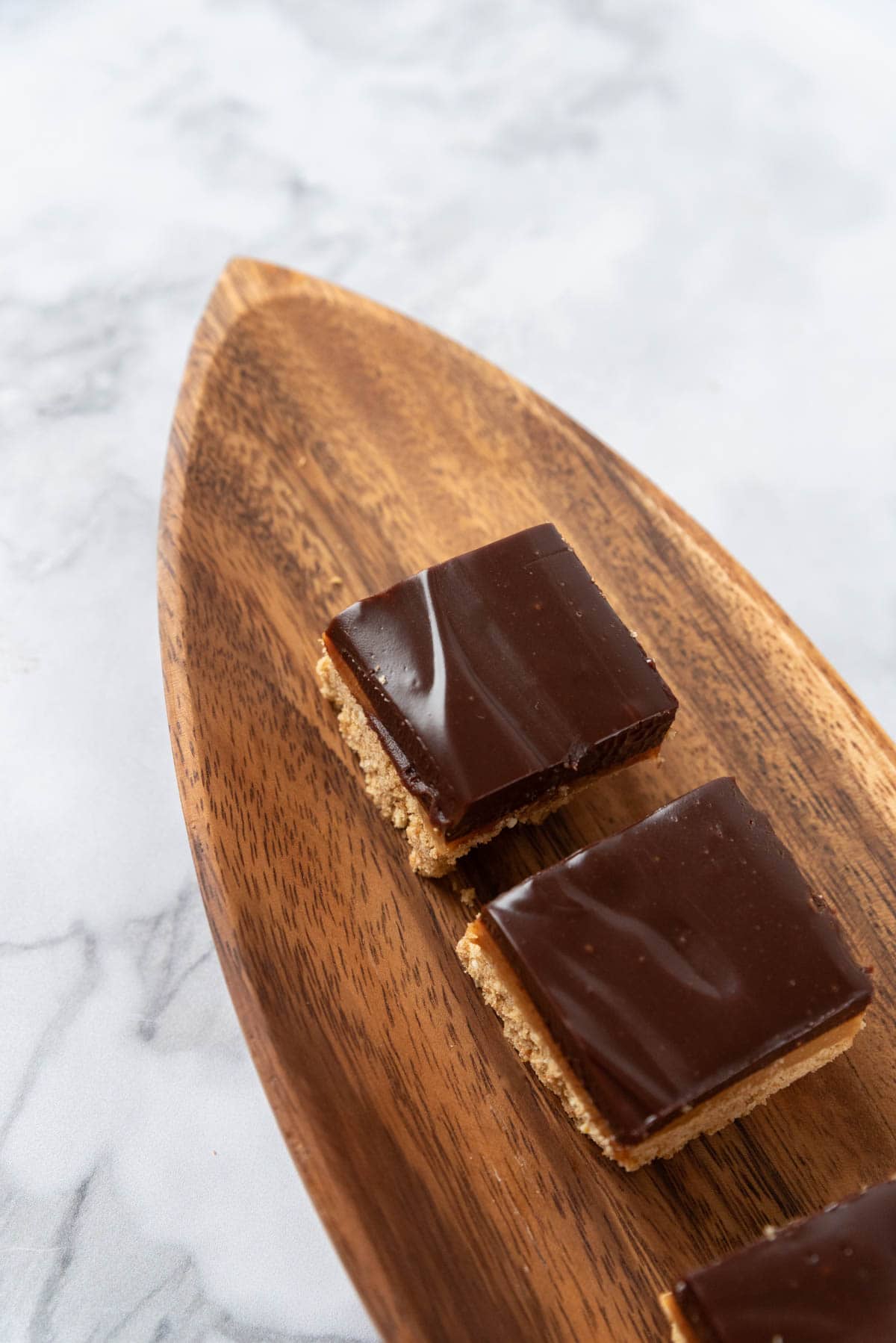 A closeup of beautiful, glossy chocolate espresso bars on a wooden serving platter.