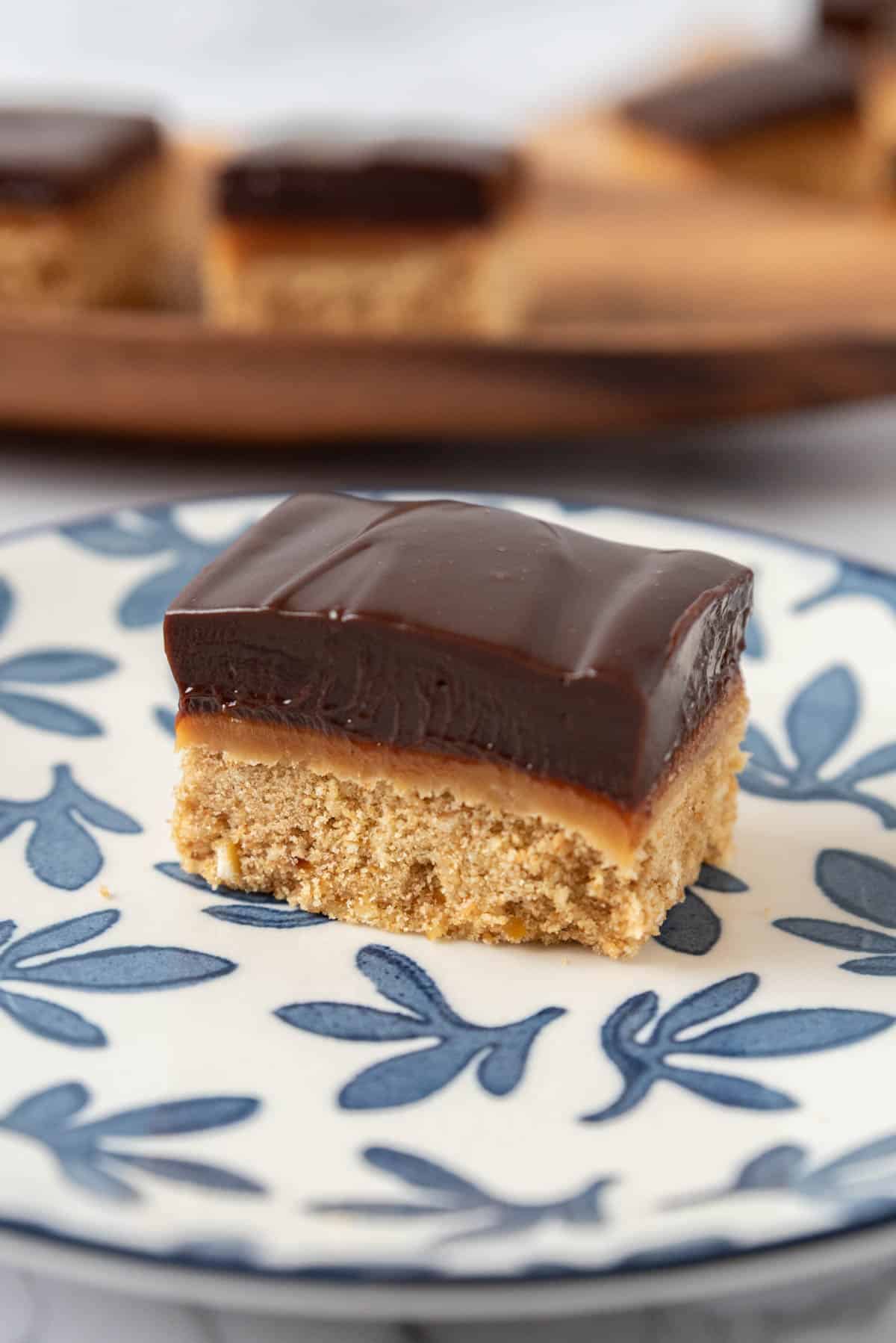 A closeup of a chocolate espresso bar on a white plate with delicate blue leaves. A wooden serving platter in the background.