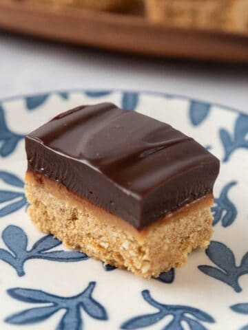 A closeup of a chocolate espresso bar on a white plate with delicate blue leaves. A wooden serving platter in the background.