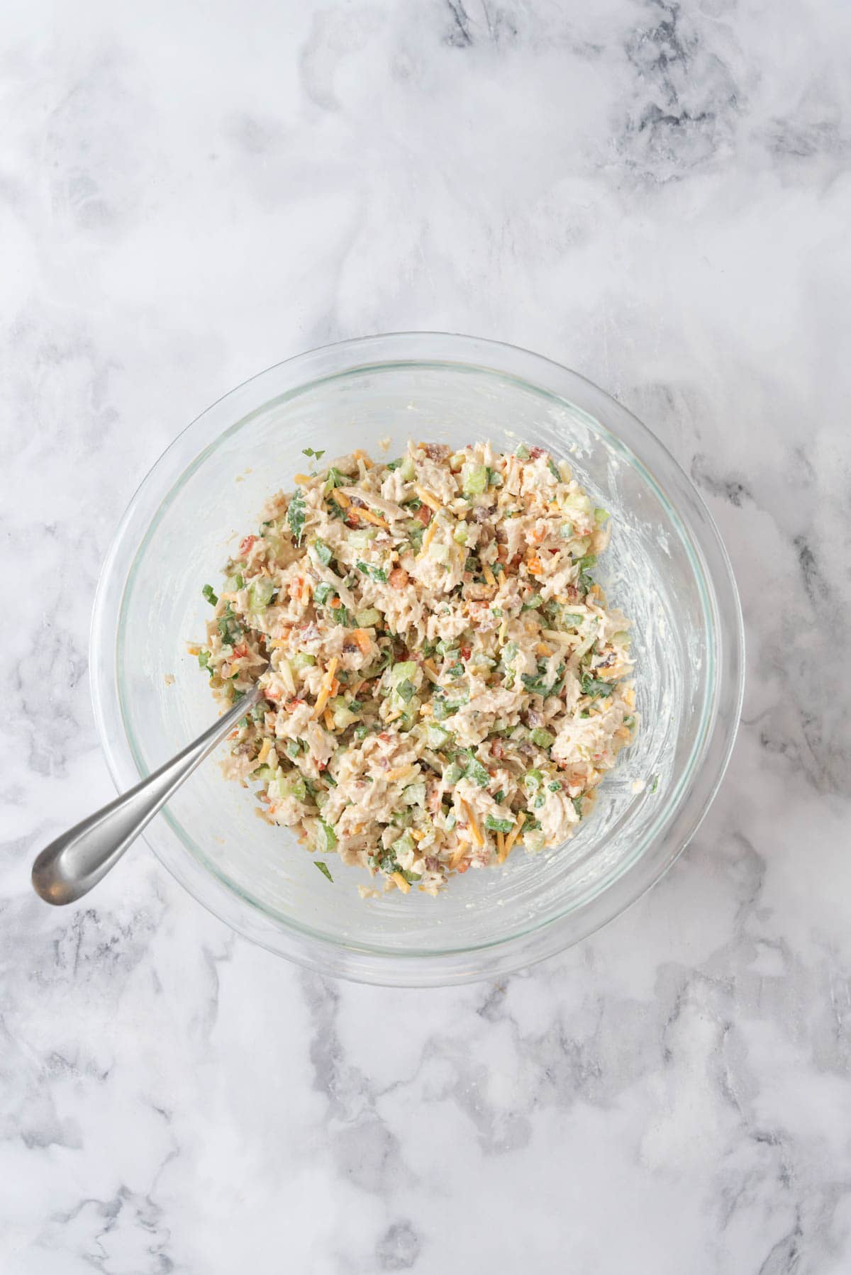 Jalapeno chicken salad mixed together in a medium glass mixing bowl with a large fork in the bowl. The bowl rests on a white and grey marble countertop.