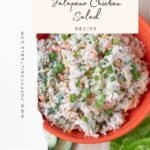 A bright orange bowl loaded with Jalapeno Chicken Salad. Flecks of cheese, peppers, cilantro and green onion visible in the salad. The bowl rests on a wooden board along with pita bread, lettuce leaves, sliced veggies, crackers and a small wooden bowl. Poppy Trail Table graphic overlayed for Pinterest.