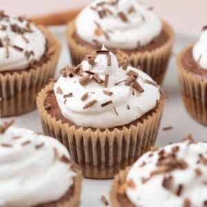Mini chocolate cheesecakes topped with whipped cream and shaved chocolate resting on a serving platter.
