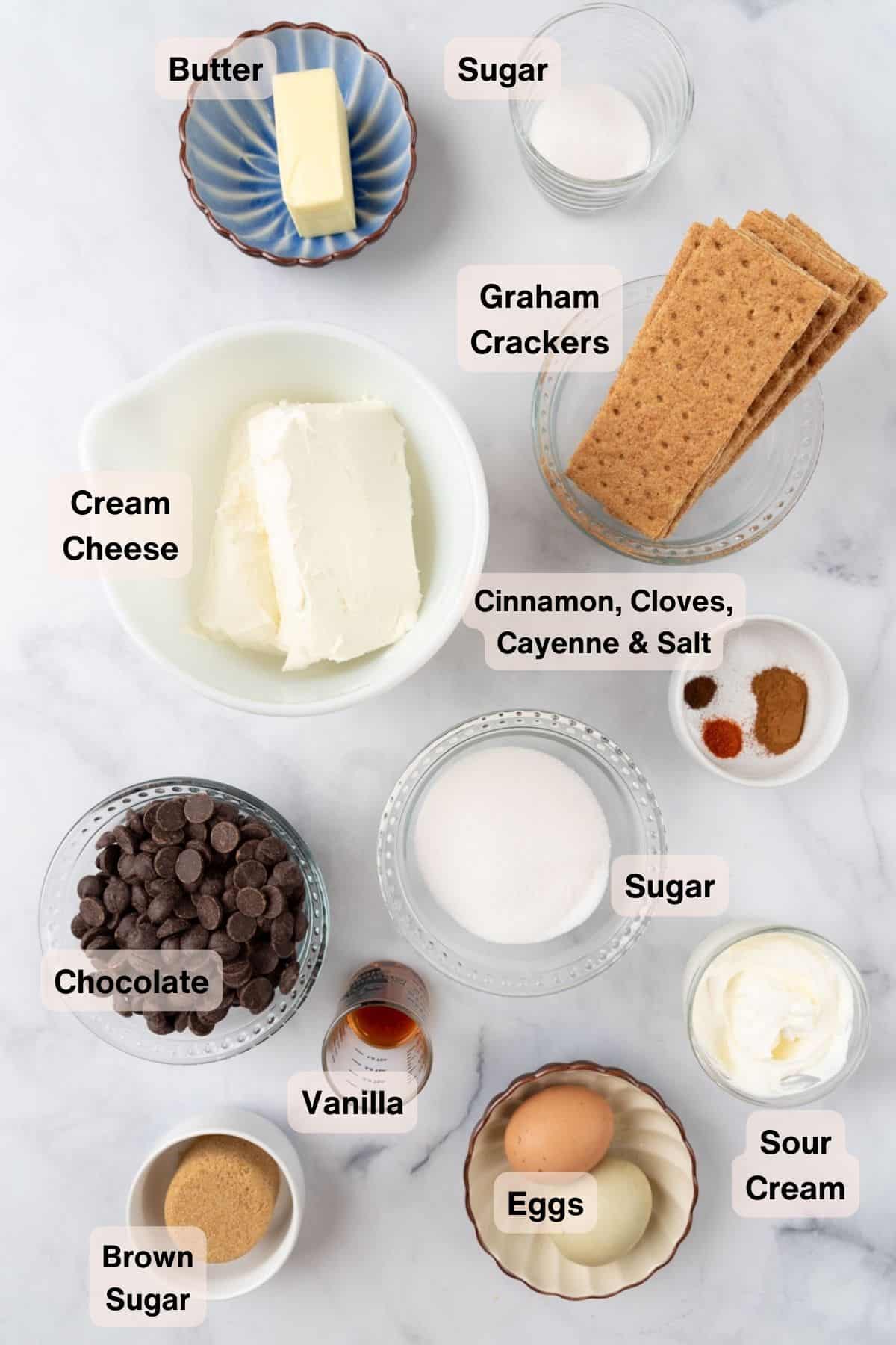 Ingredients for Mini Mexican Hot Chocolate Cheesecakes labeled and spread across a white marble countertop.