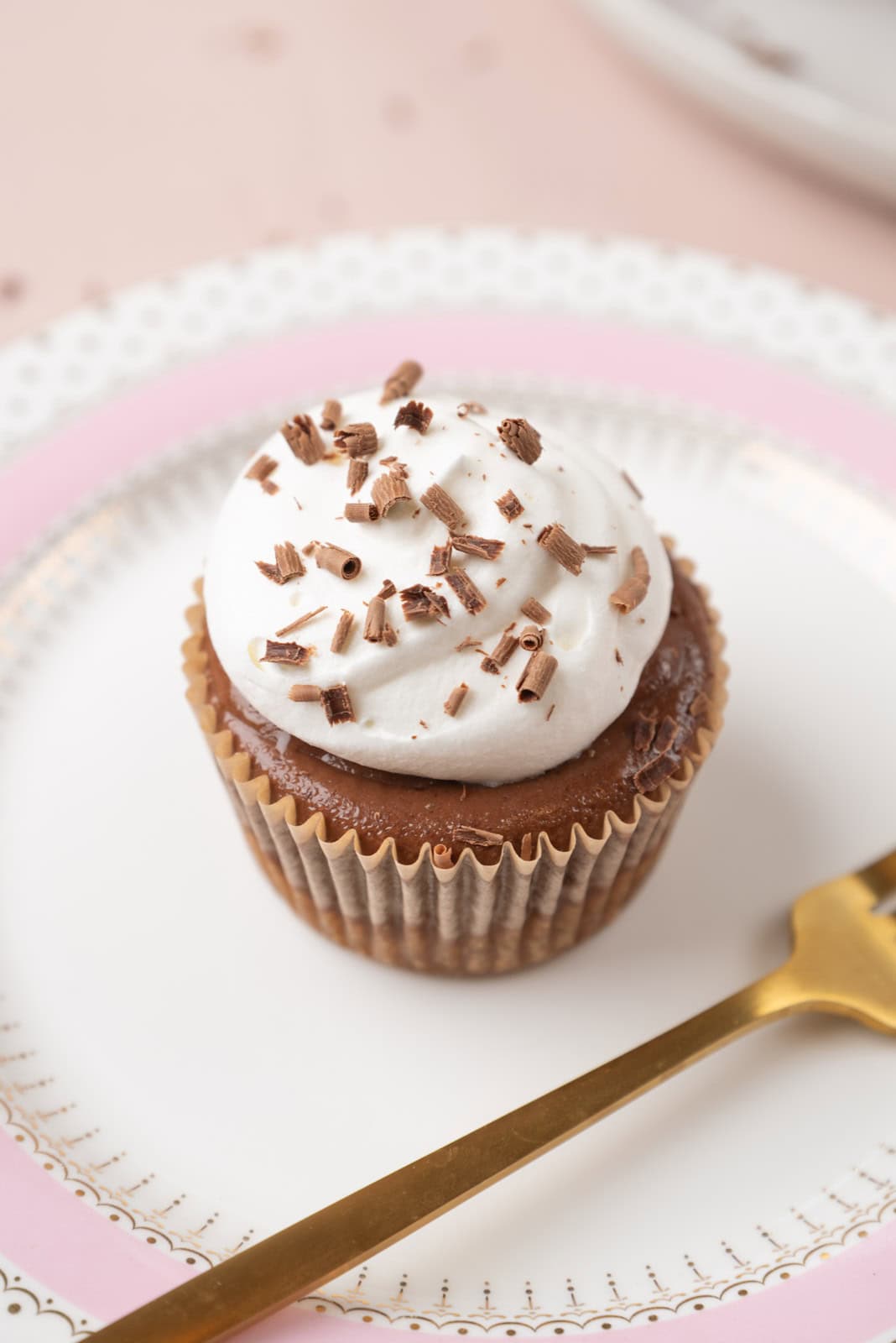 A closeup of one mini Mexican hot chocolate cheesecake on a pink and gold dessert plate with a gold fork, resting on a pale pink tabletop.