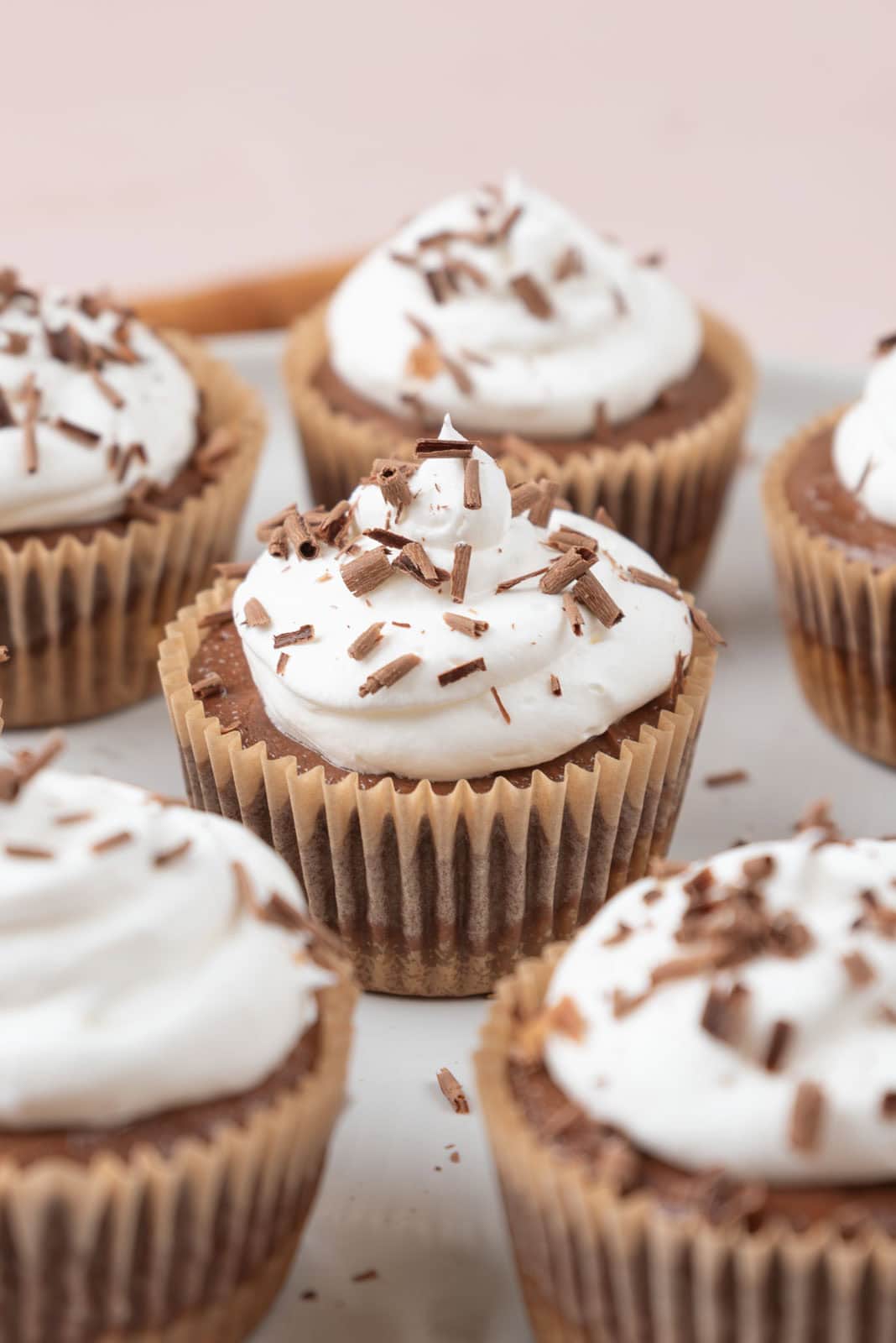 Mini chocolate cheesecakes topped with whipped cream and shaved chocolate resting on a serving platter.