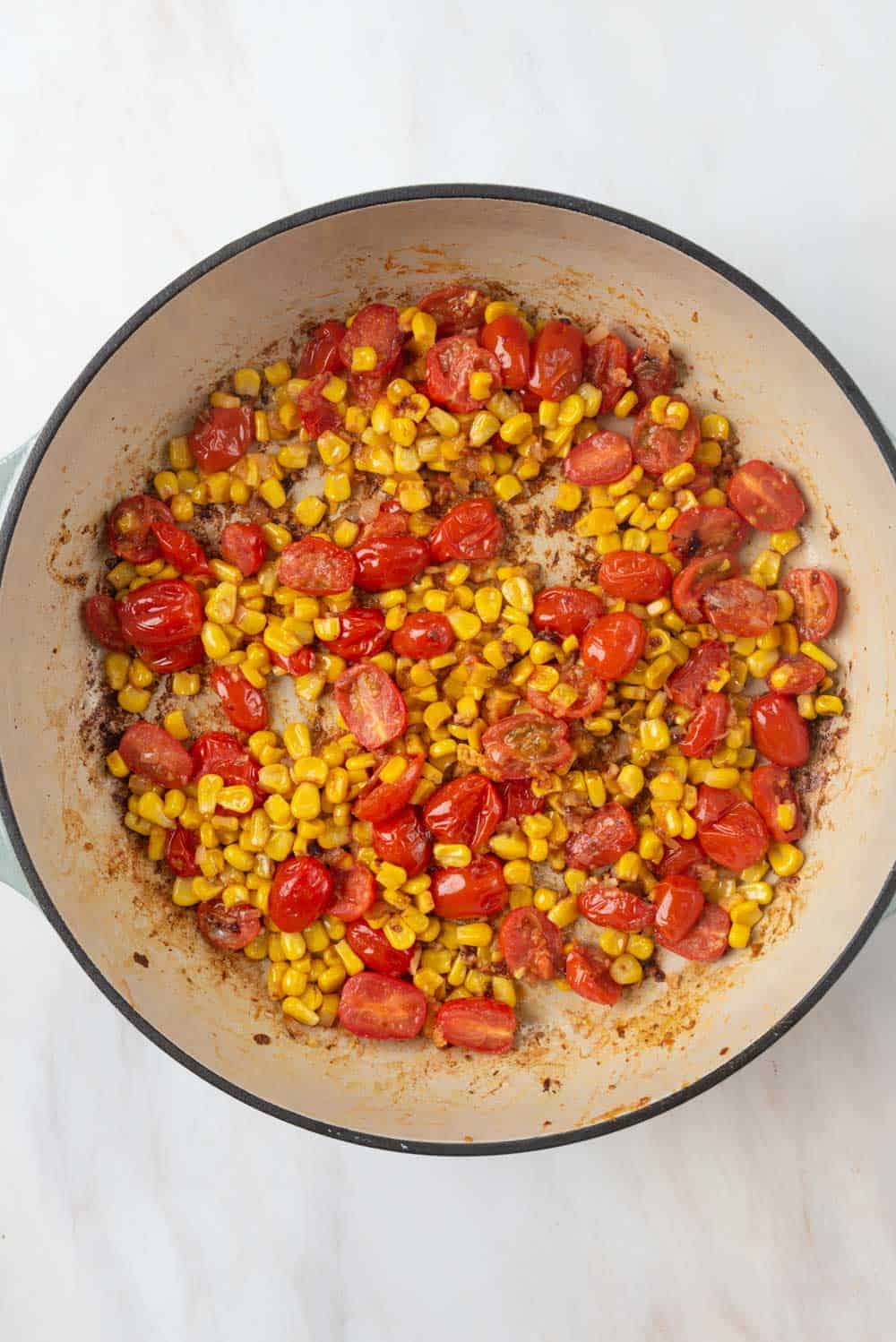 Blistered cherry tomatoes cooked down with corn in a braising pan.