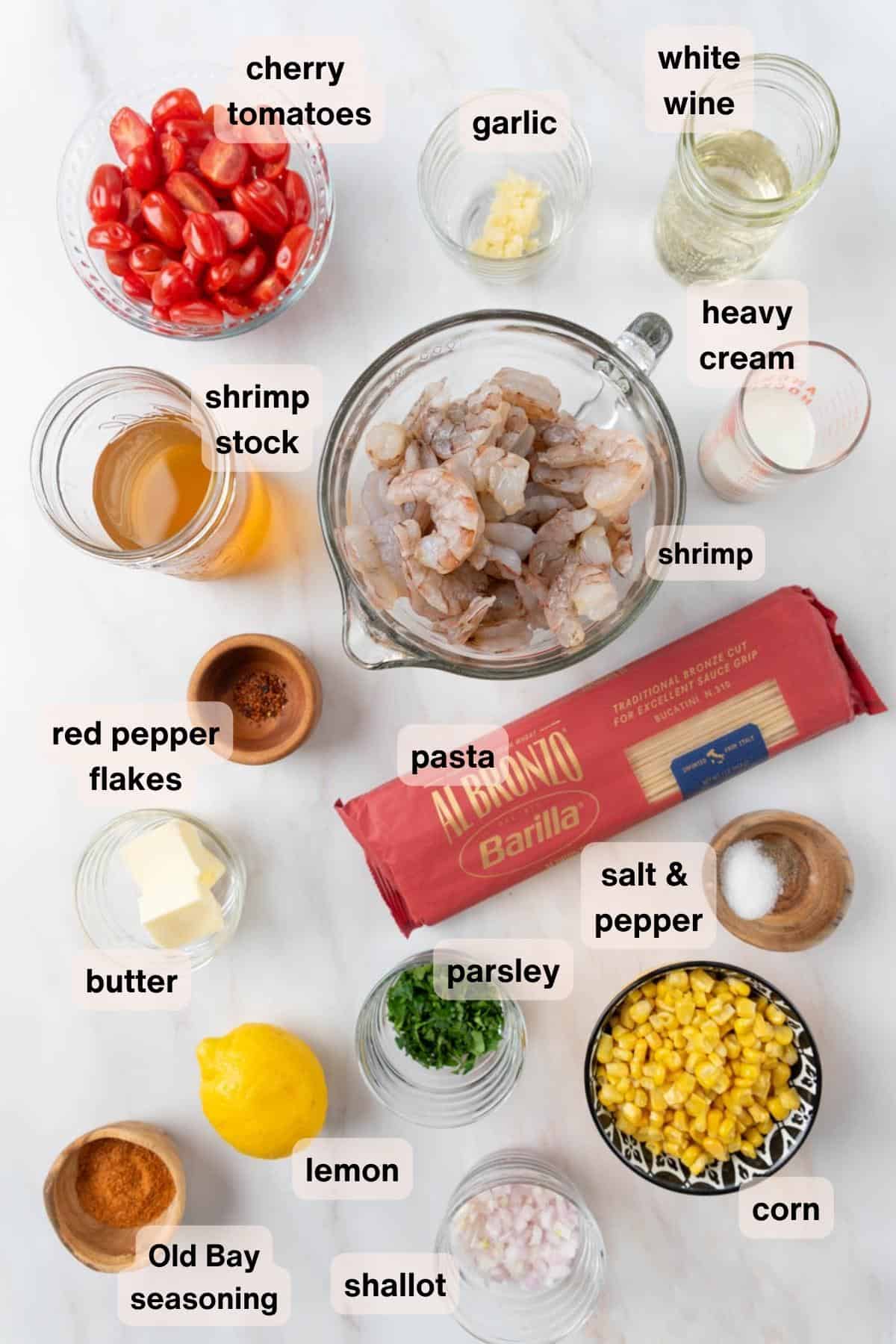 All ingredients for Old Bay Shrimp Pasta in various dishes and bowls spread out on a white marble countertop.