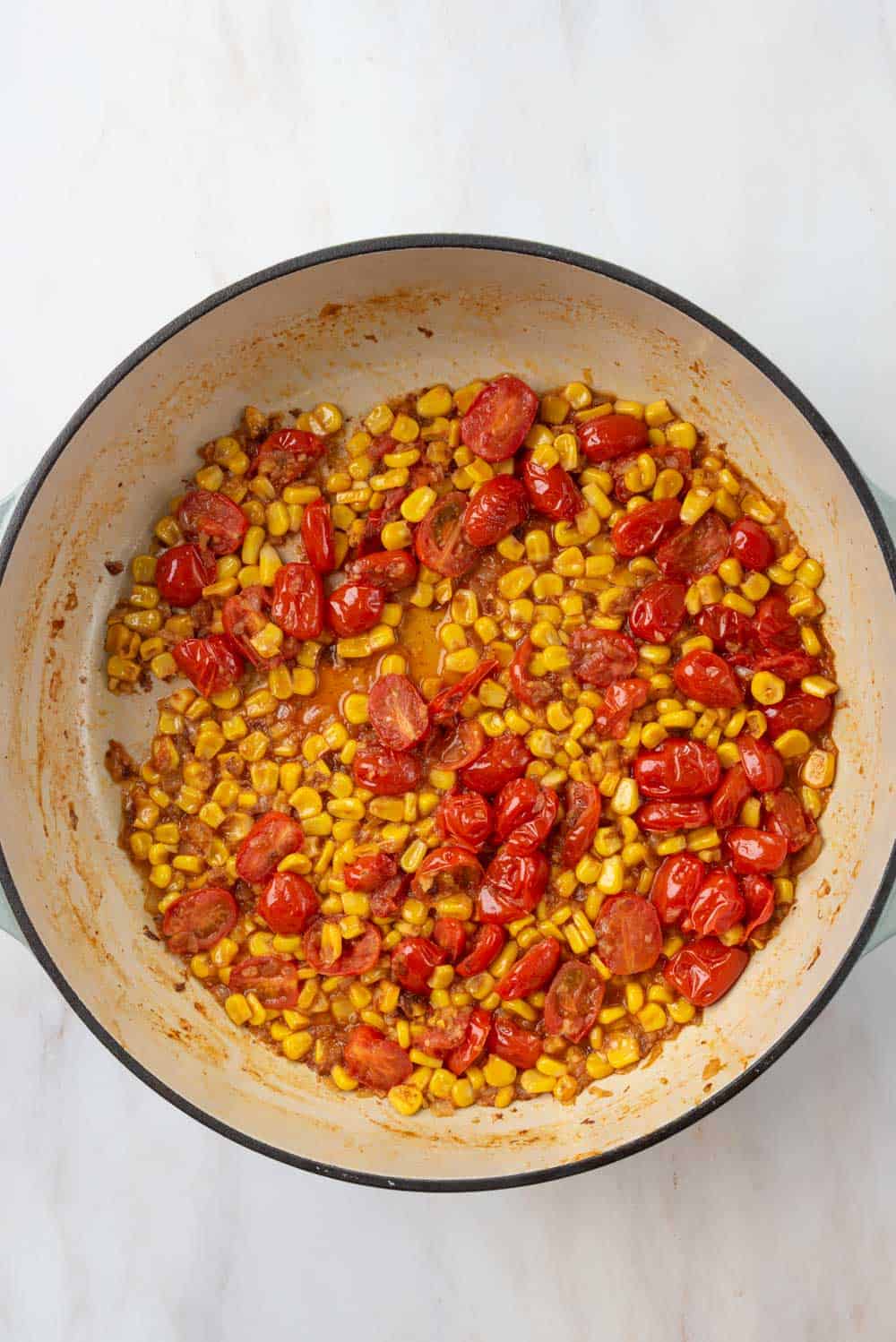 A braising pan holding aromatics, blistered cherry tomatoes and corn with wine added to deglaze the frond on the skillet bottom.
